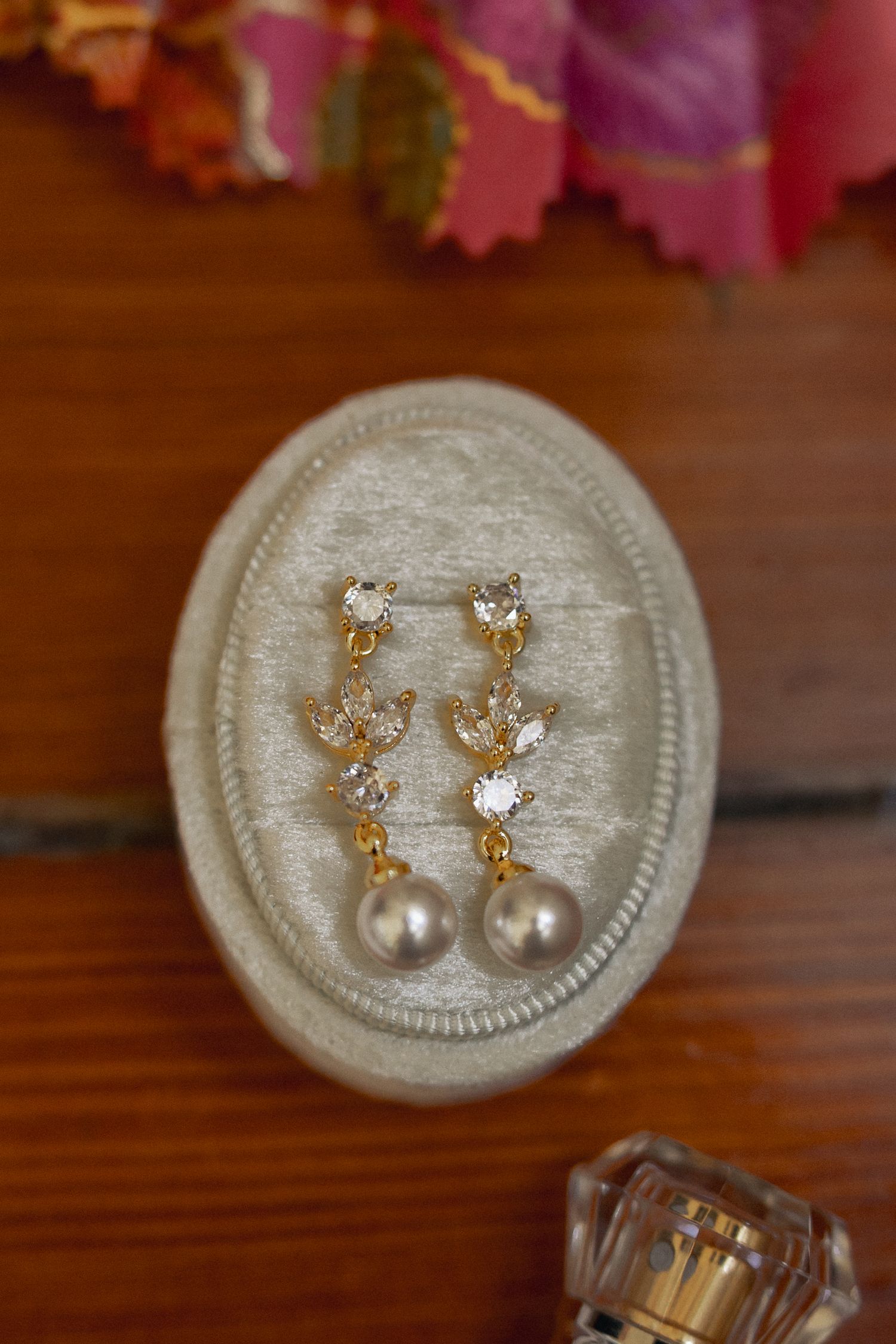 Elegant gold crystal and pearl drop earrings displayed on an oval gray velvet jewelry tray on wooden surface.