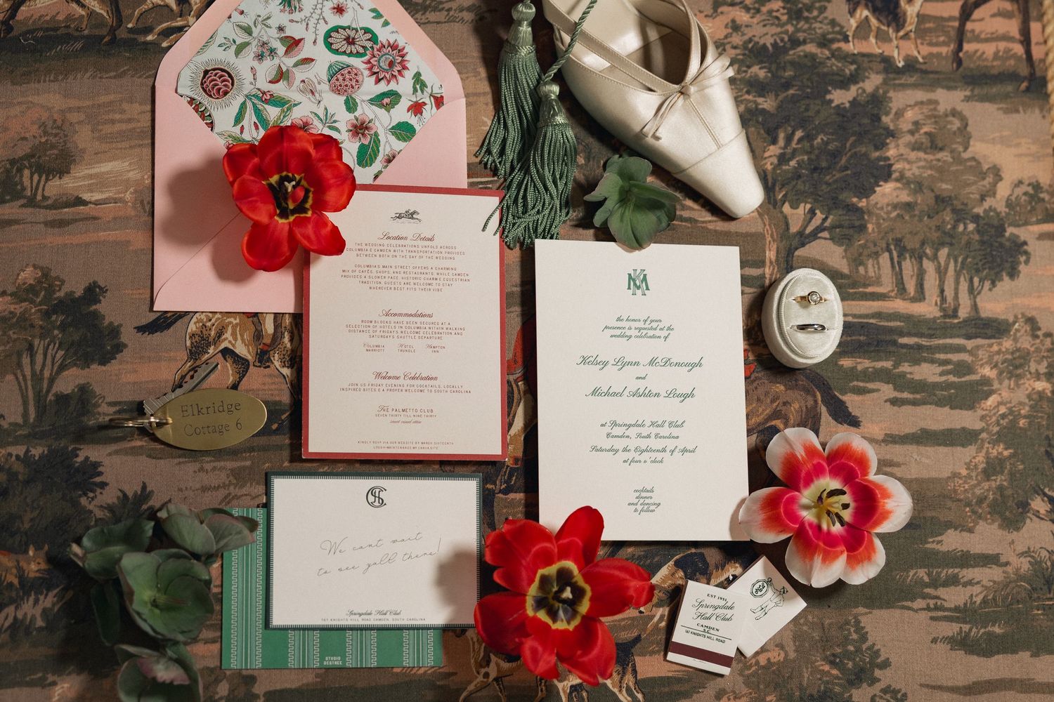 Elegant wedding invitation suite with red tulips, green accents, pink floral envelope, and silver heels on vintage backdrop.