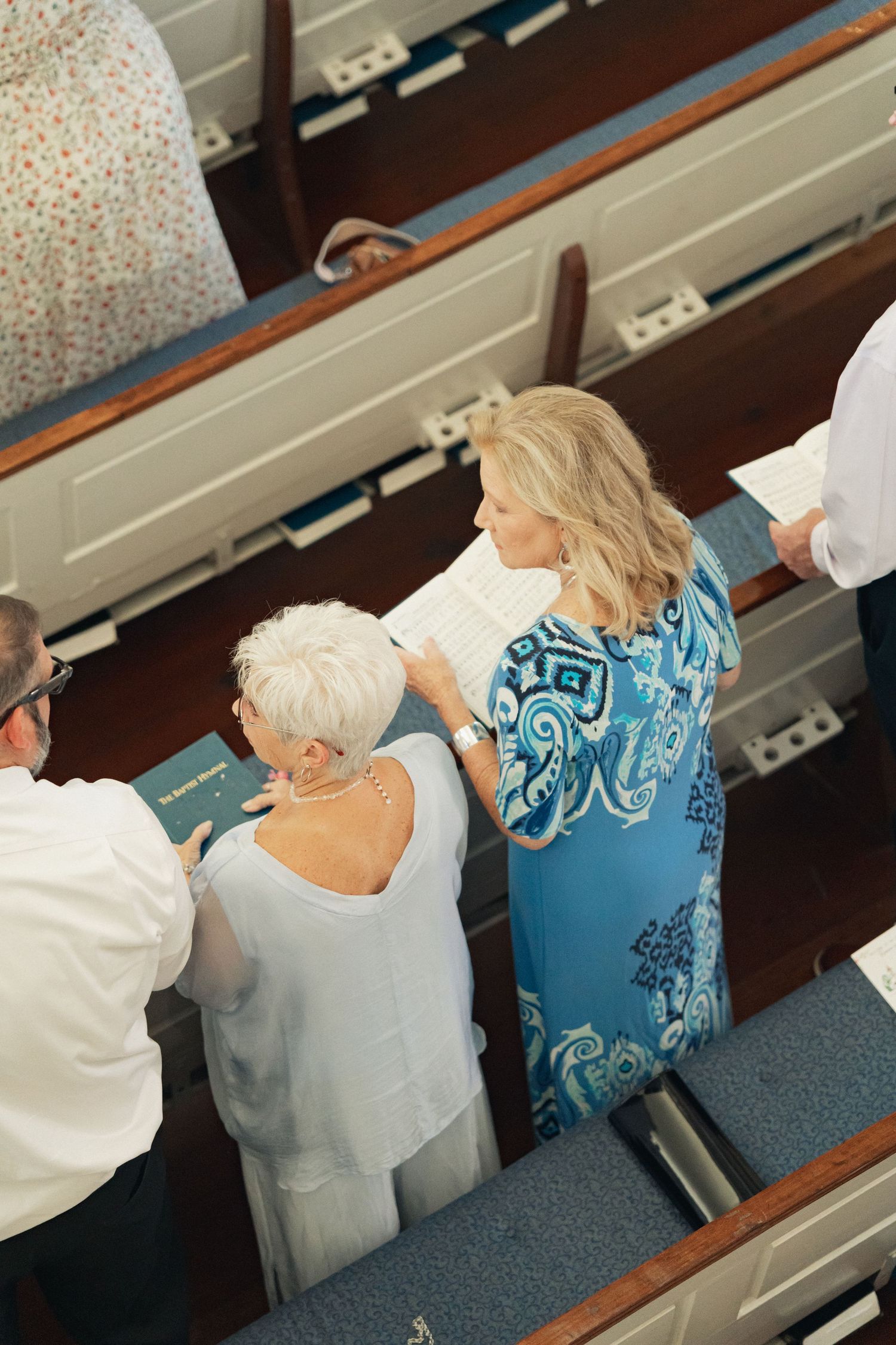 Overhead view of wedding guests standing in church pews, reading from programs during a ceremony.