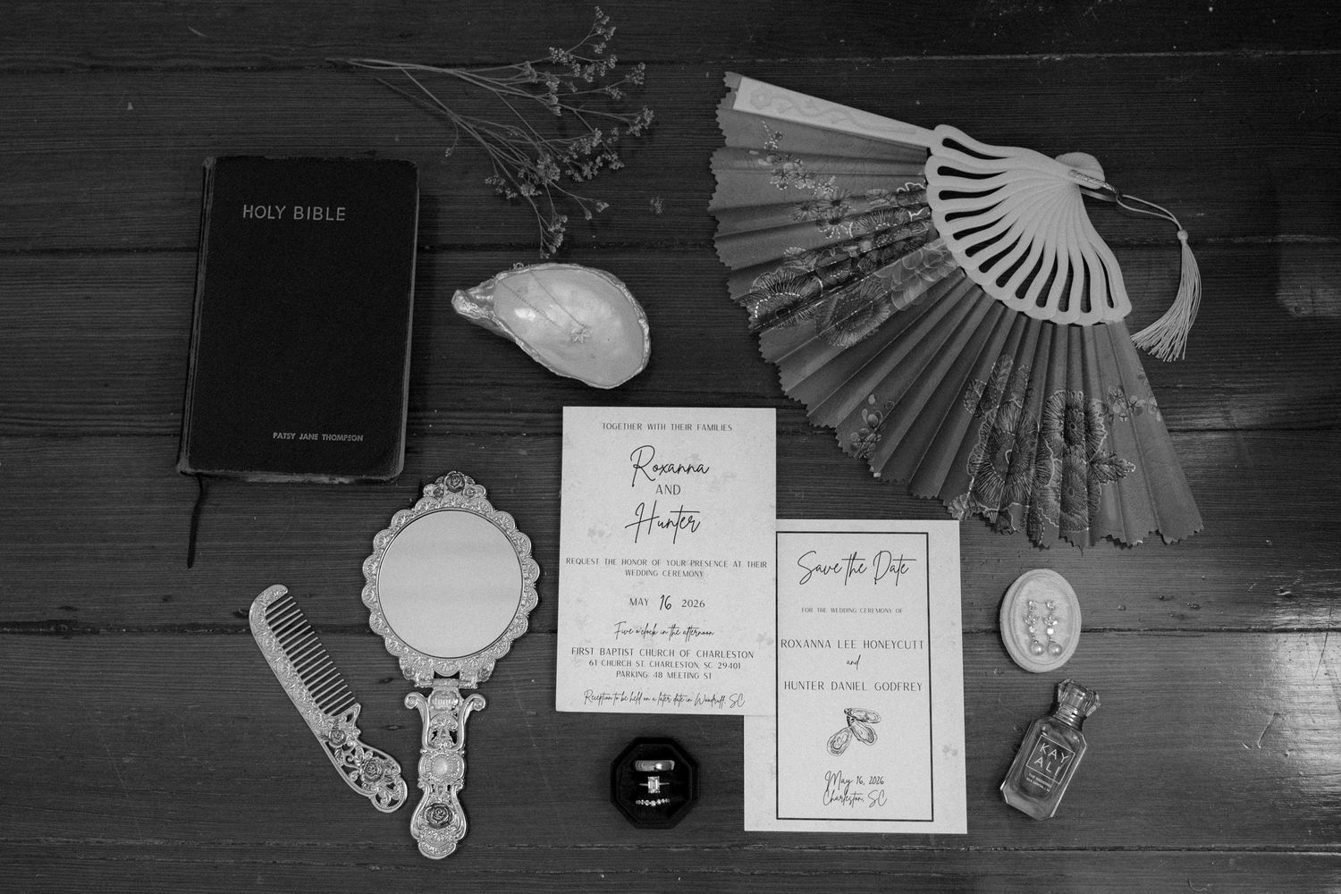 Black and white flat lay of wedding stationery, Bible, fan, and vintage accessories.