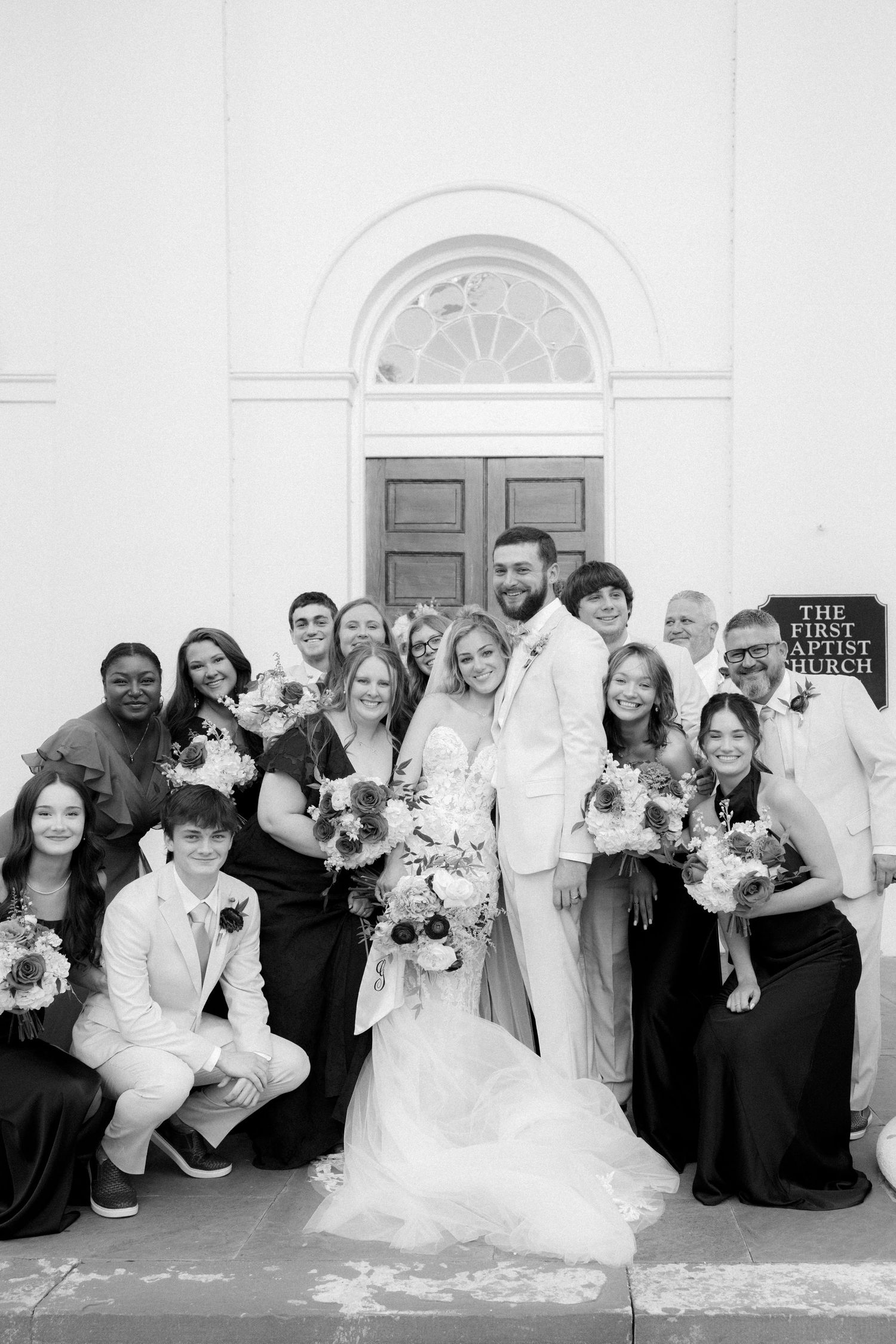 Black and white wedding photo of bride, groom, and guests posing outside First Baptist Church.