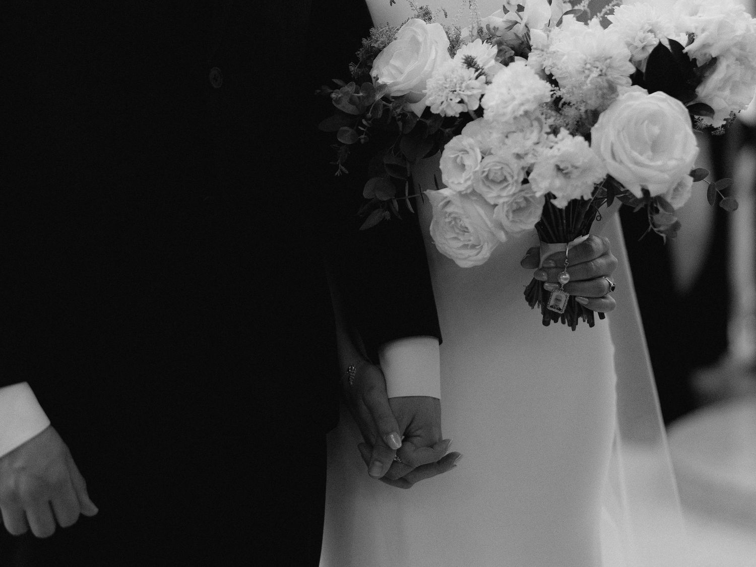 Black and white photo of bride and groom holding hands with white rose wedding bouquet.