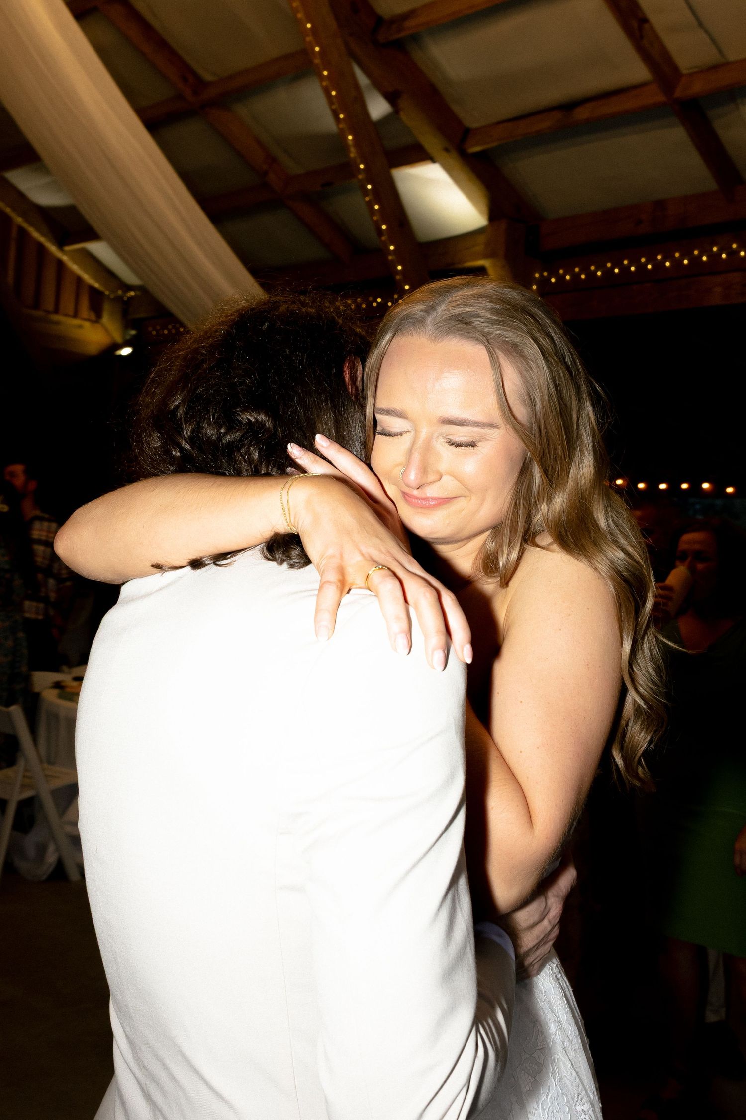 Bride and groom sharing romantic first dance kiss at rustic barn wedding with string lights.