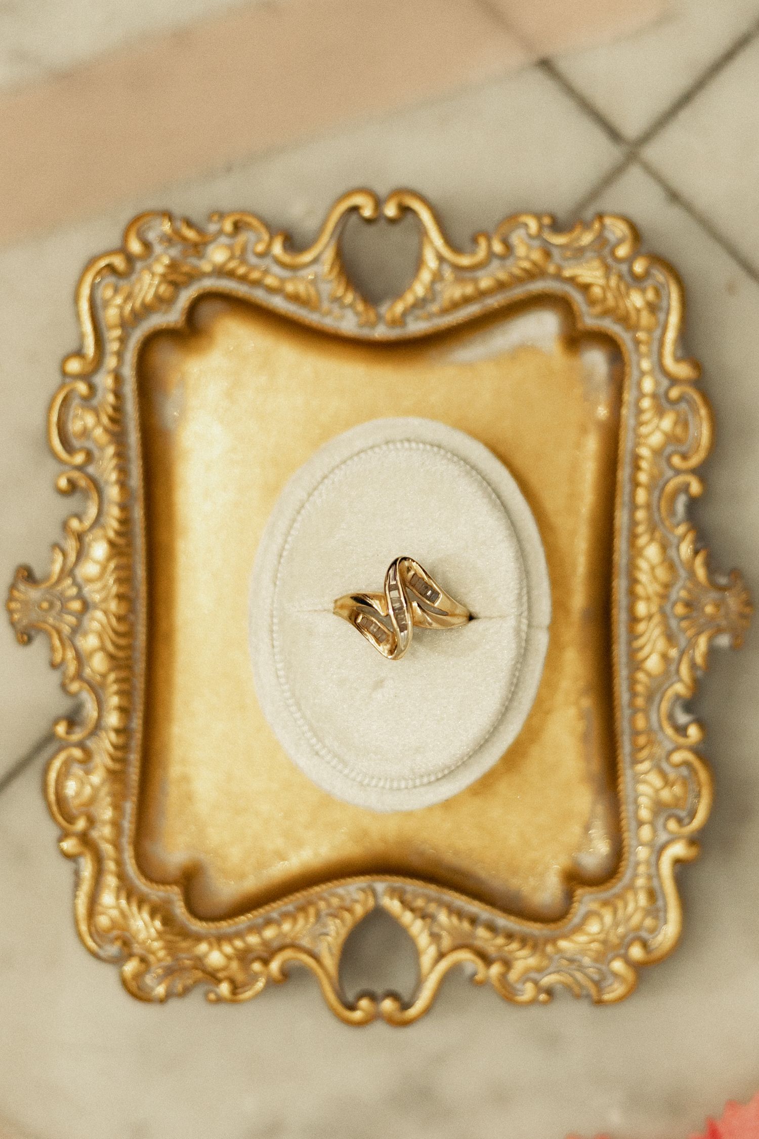 Gold butterfly ring displayed on cream velvet oval stand inside ornate vintage golden baroque picture frame.