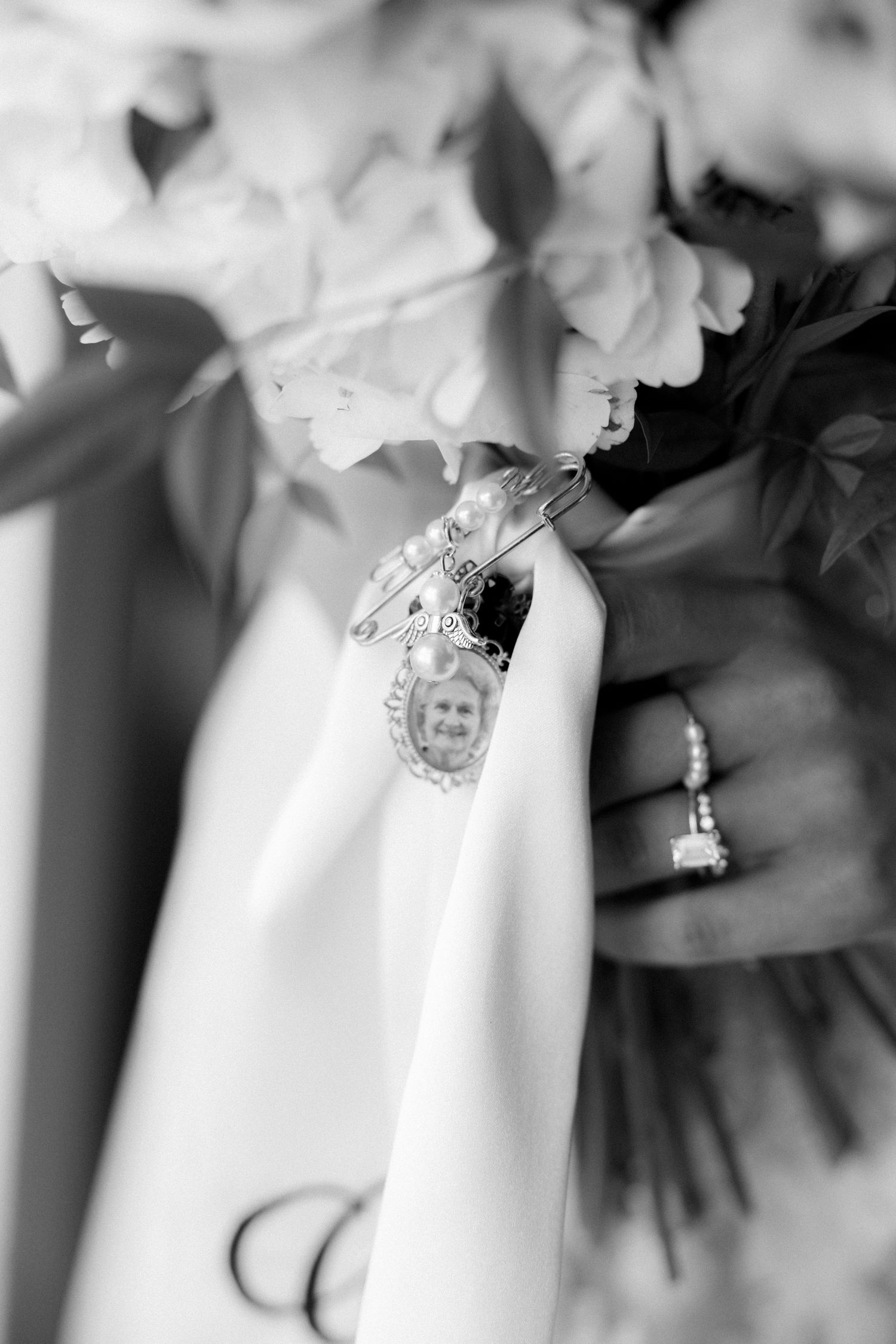 Black and white photo of bridal bouquet with memorial photo charm and diamond engagement ring.