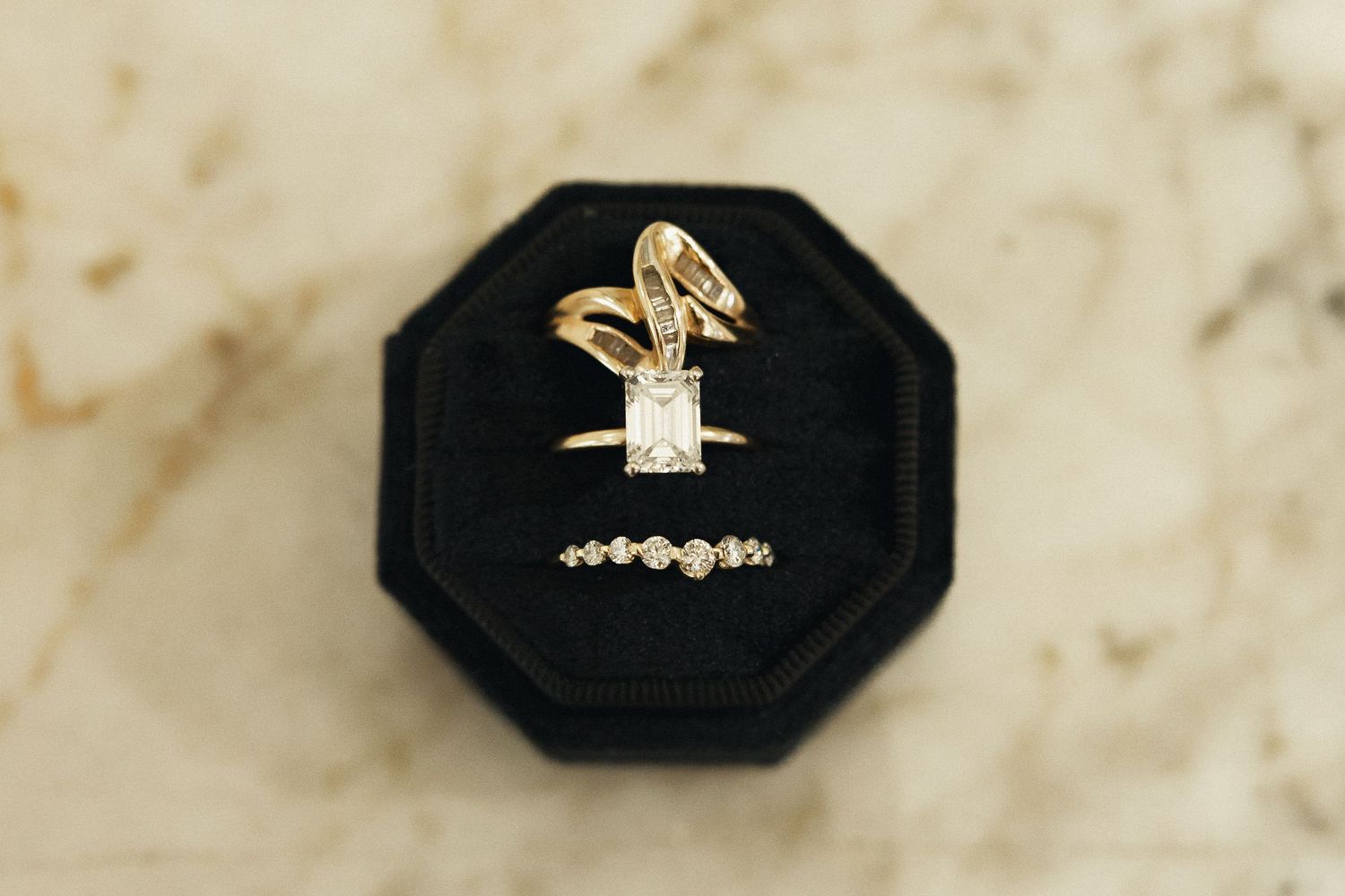 Gold engagement ring with emerald-cut diamond and matching wedding band displayed in black velvet ring box.