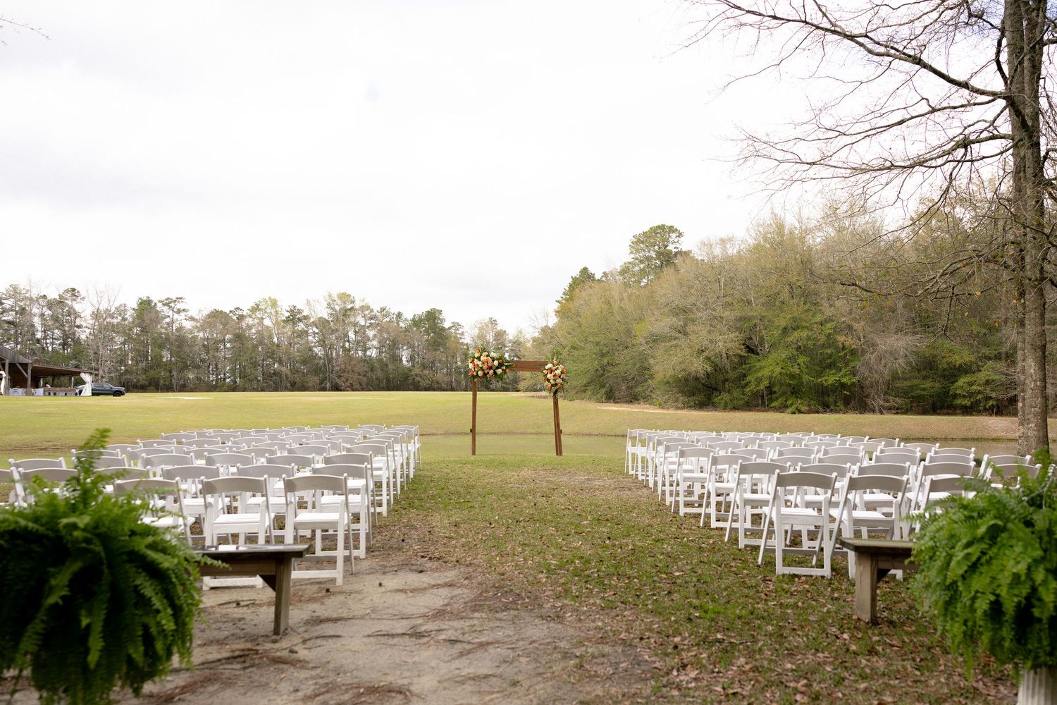 Outdoor wedding ceremony setup with white chairs arranged in rows on green grass with a wooden arch centerpiece.
