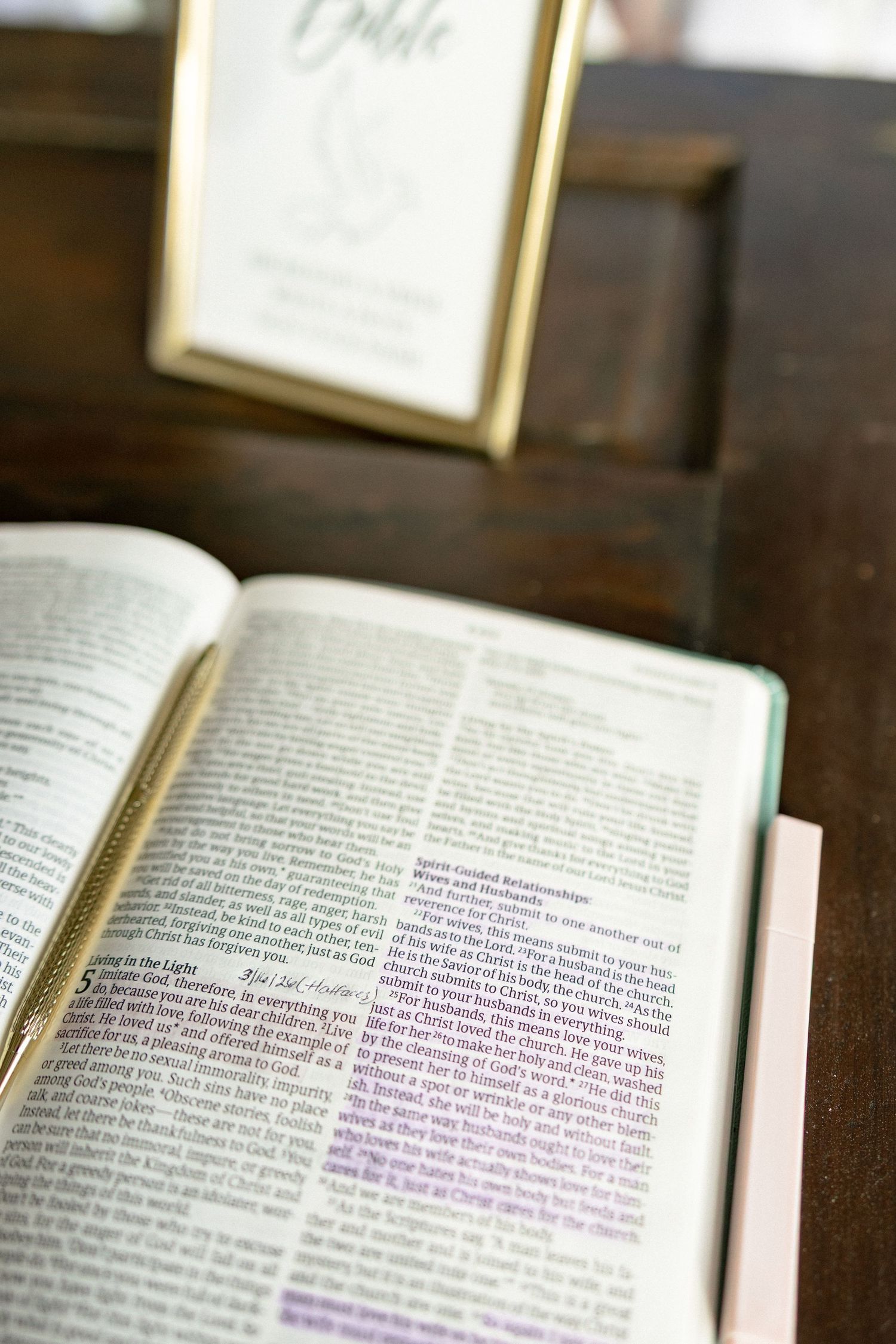 Open Bible on a dark wooden table with a gold-framed sign at a wedding ceremony.