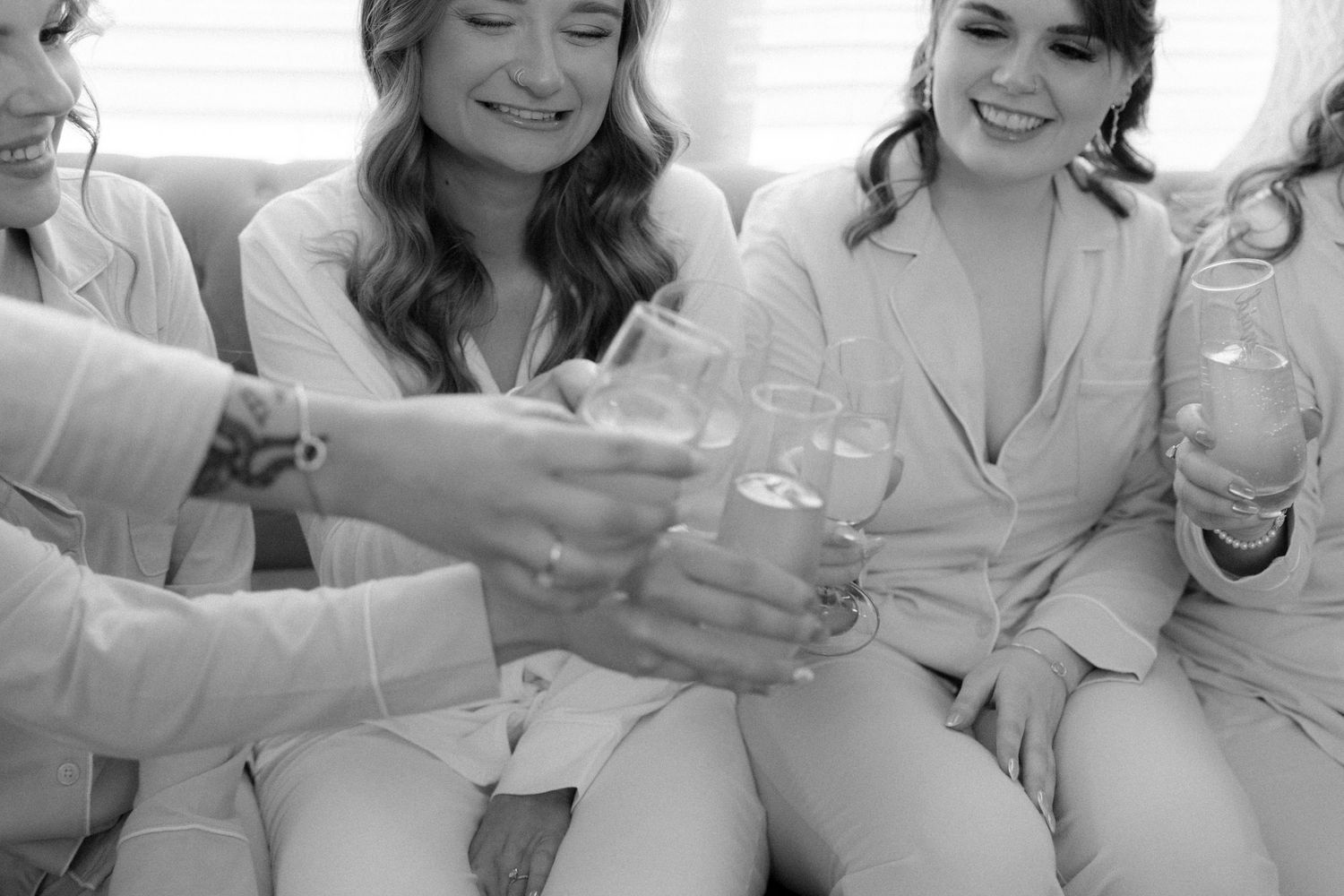 Black and white photo of bridesmaids clinking champagne glasses in satin pajamas.