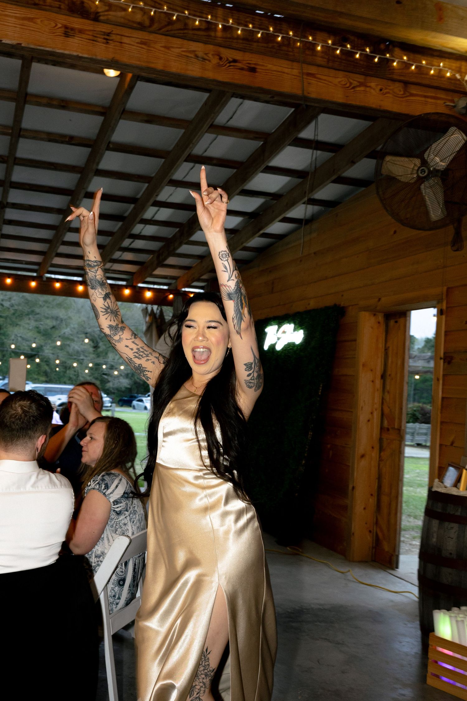 Smiling woman in copper velvet dress clapping joyfully at outdoor wedding reception at night.