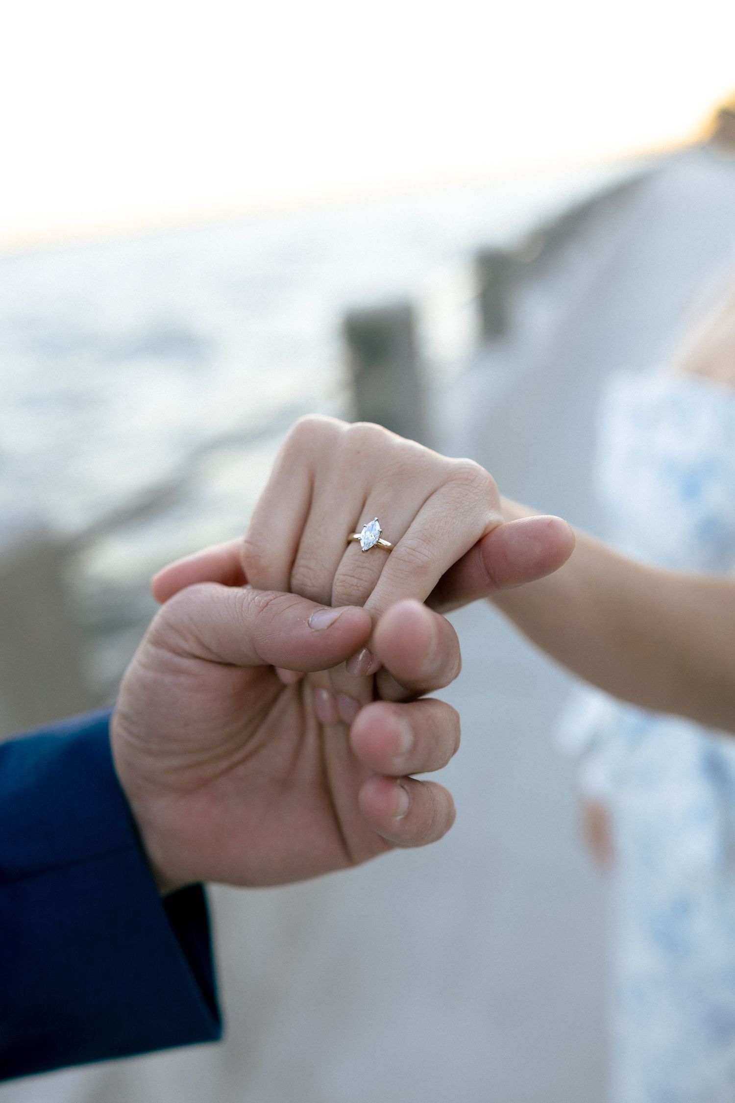 Close-up of a couple holding hands outdoors, showcasing a elegant diamond engagement ring on the woman's finger.