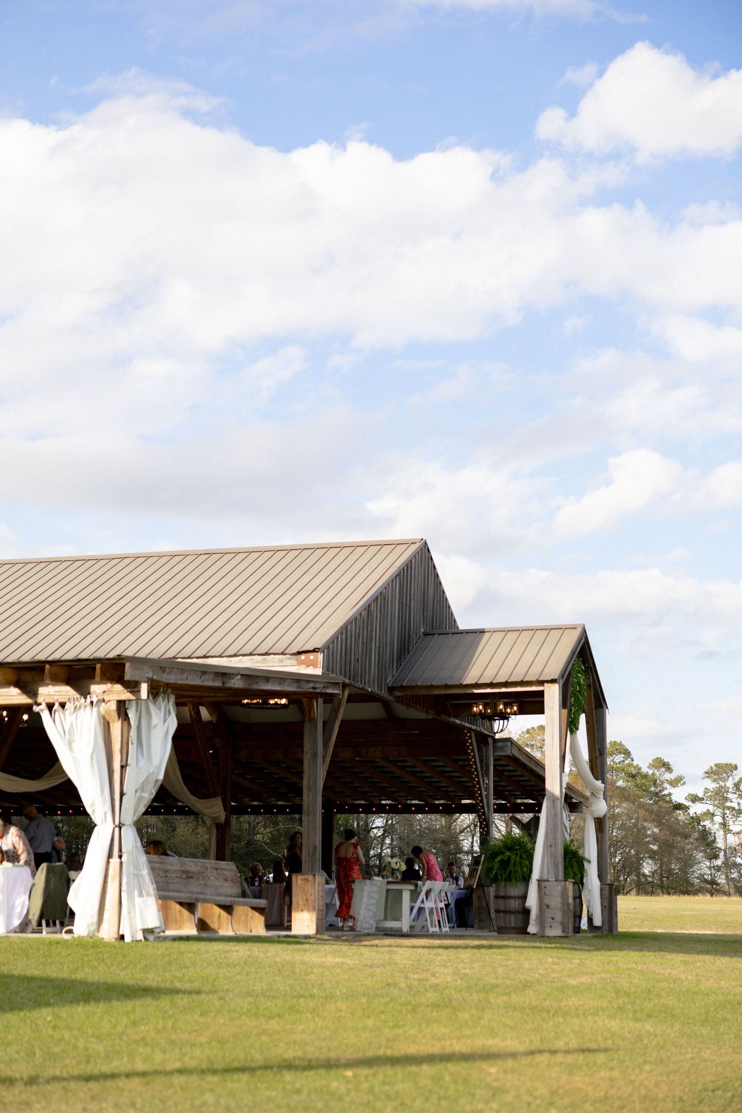 Rustic open-air barn wedding venue with white draping on a sunny day with blue skies.