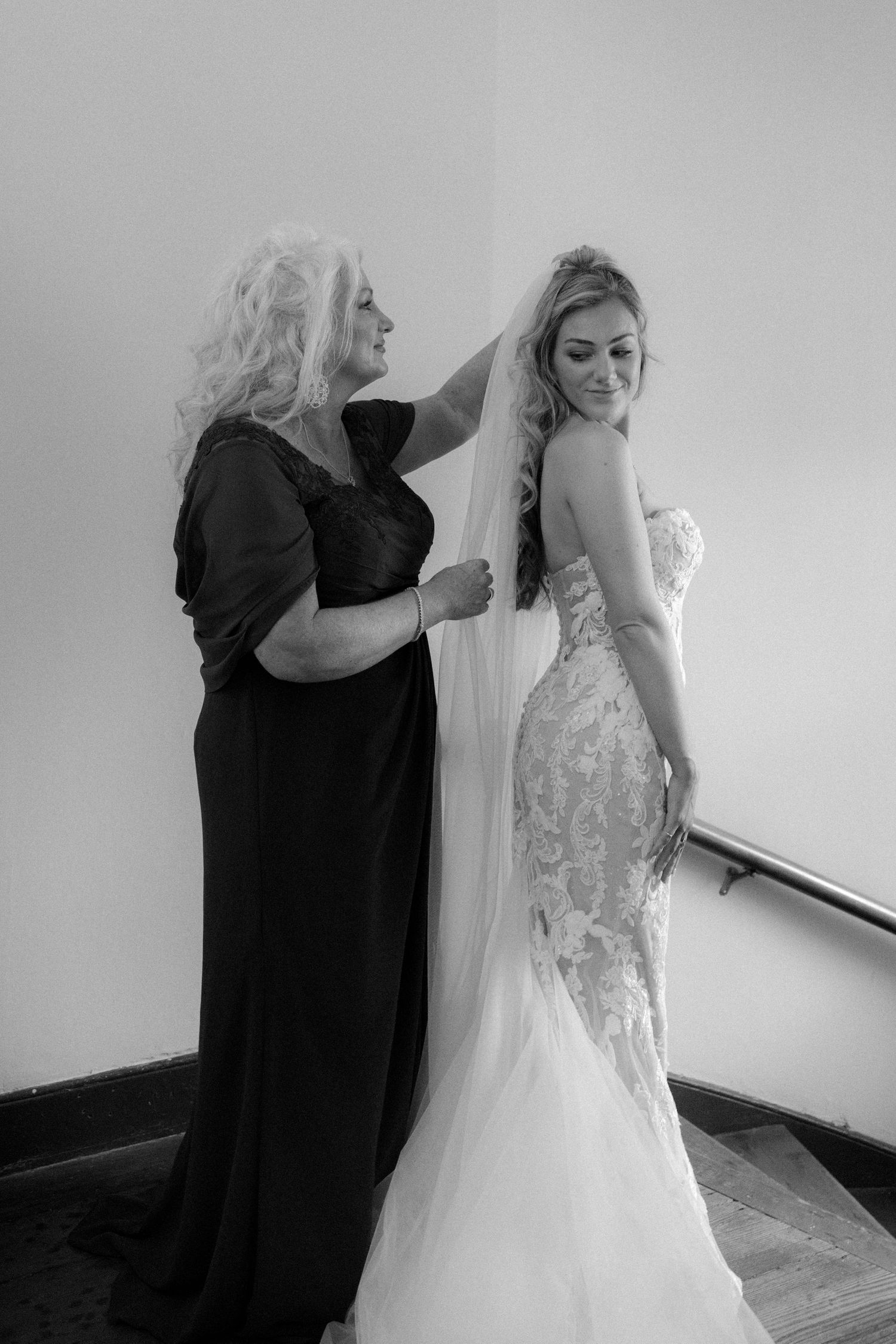Black and white photo of a mother adjusting her daughters bridal veil on a staircase.
