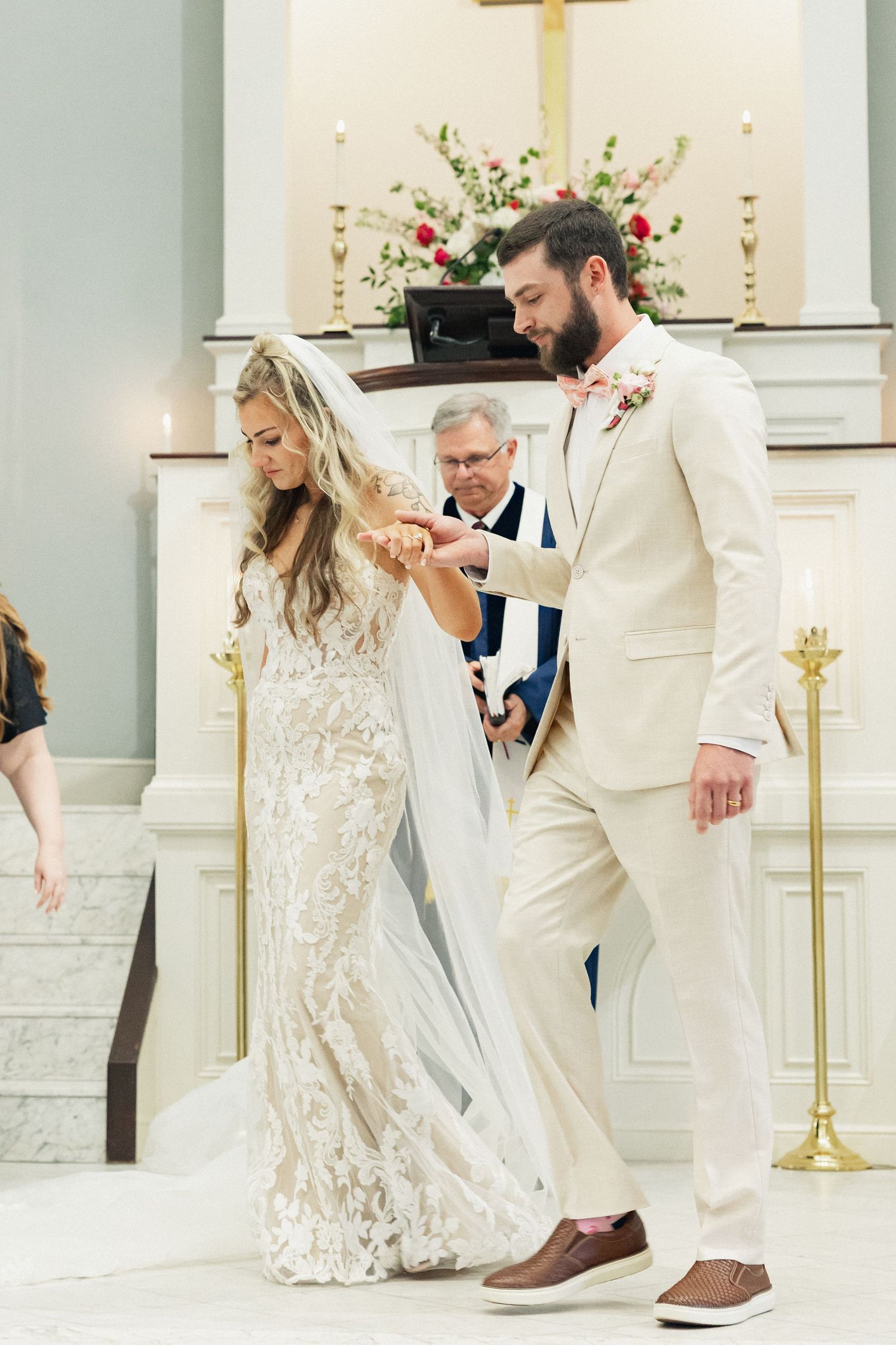 Groom in cream suit places ring on brides finger during emotional church wedding ceremony at altar.