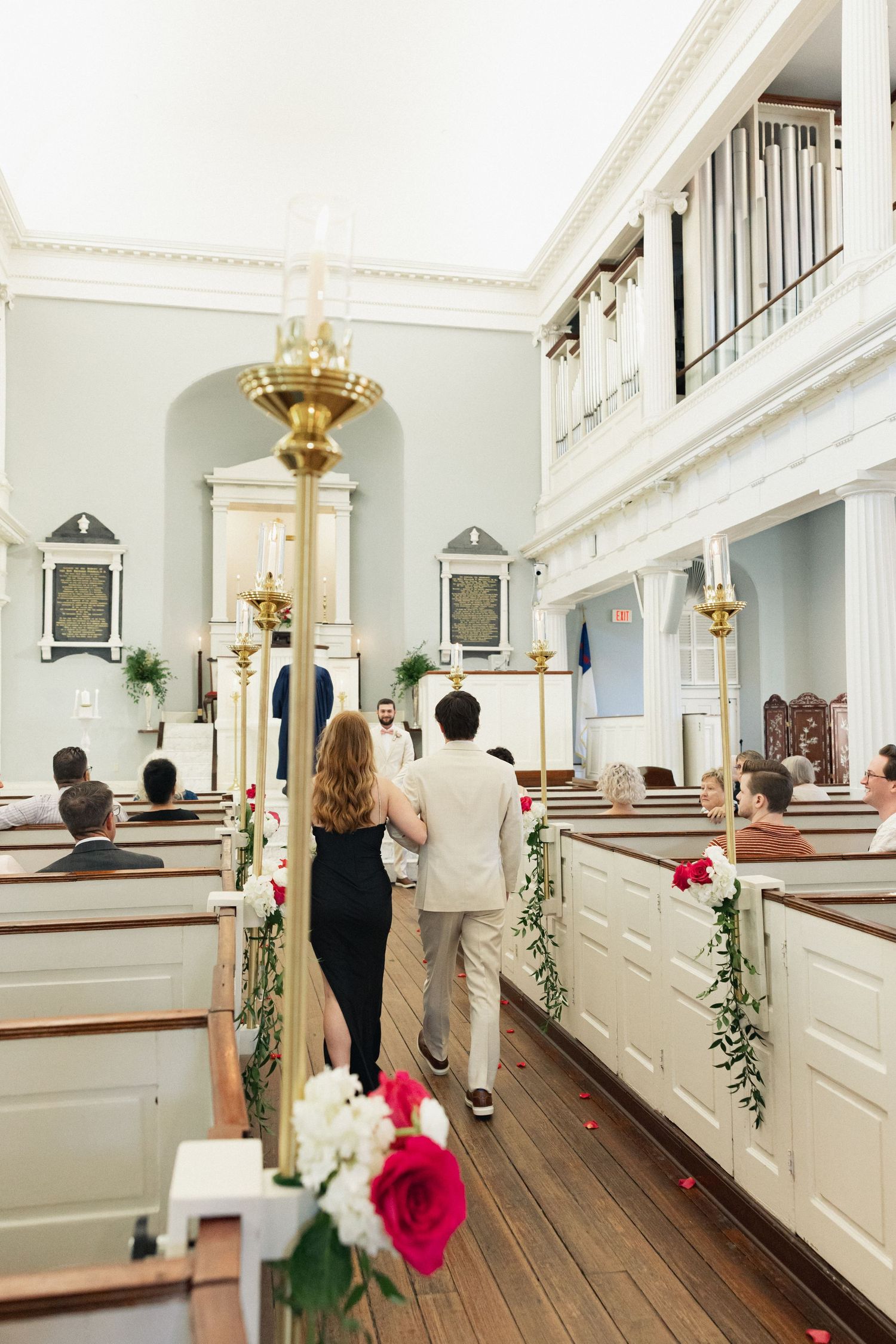 Wedding processional down the aisle of a historic church decorated with roses and greenery.