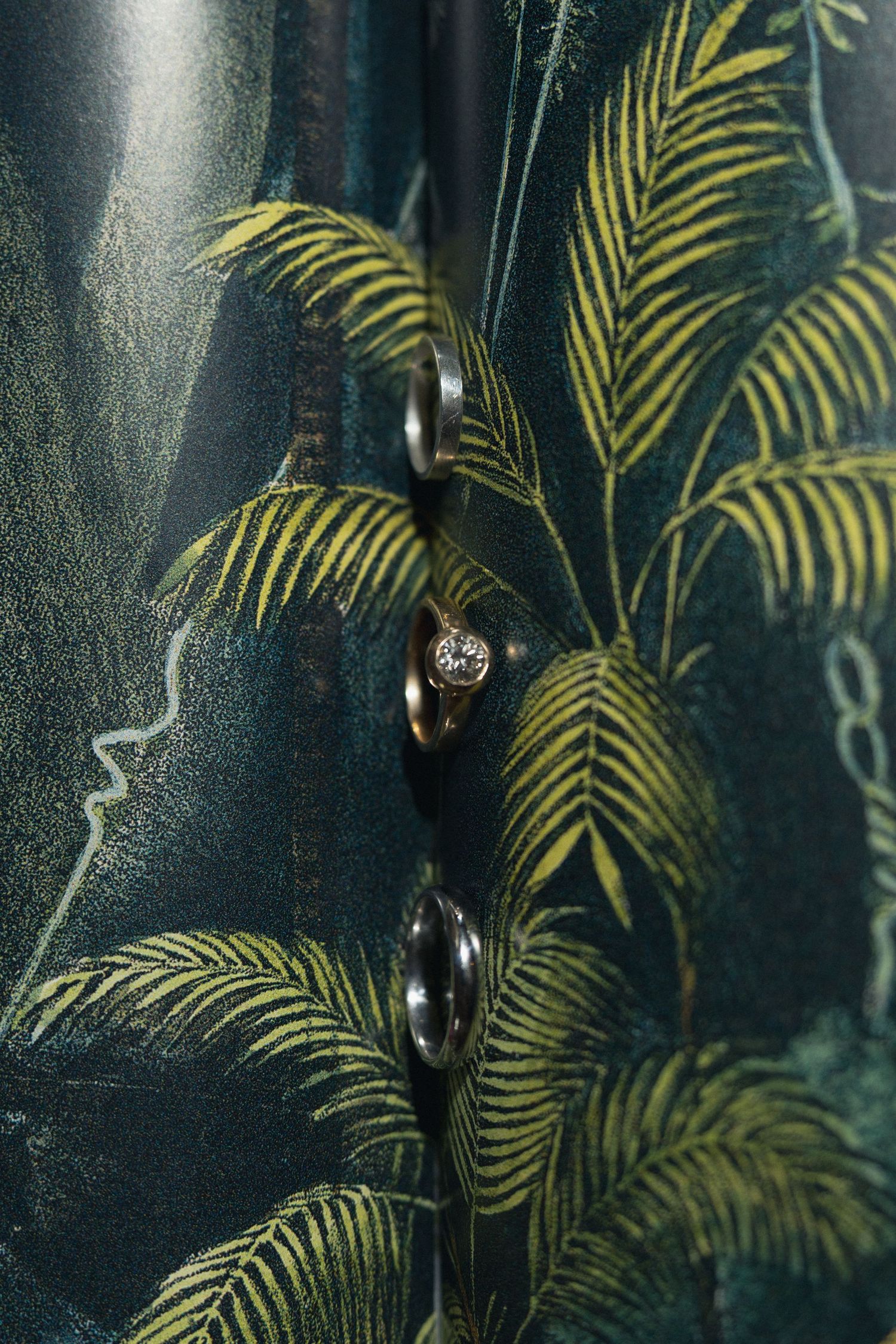 Close-up of a green tropical palm leaf print fabric with gold ring buttons and a diamond stud earring.