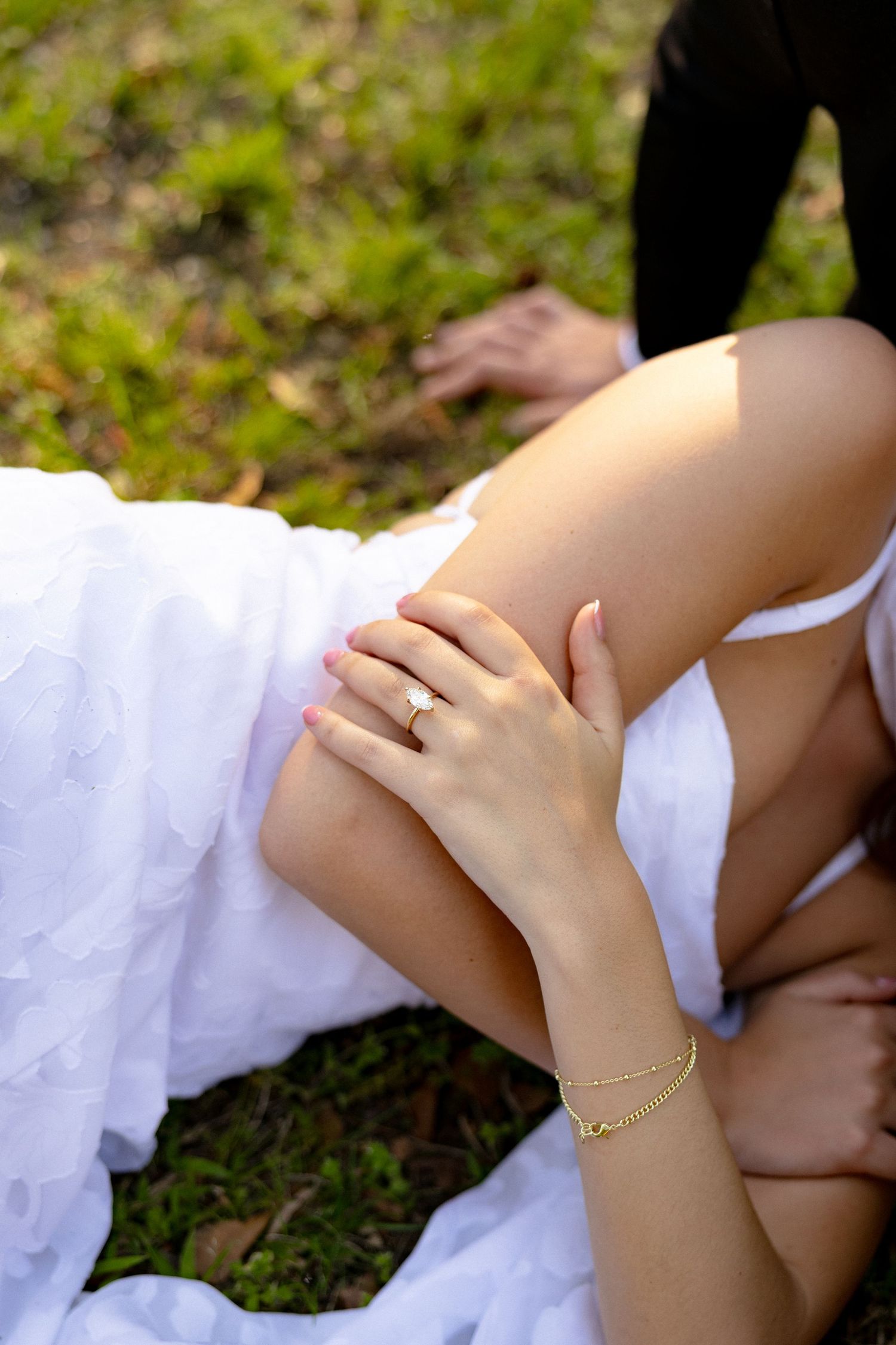 Close-up of bride's hand adorned with diamond ring and gold bracelet resting on white dress.