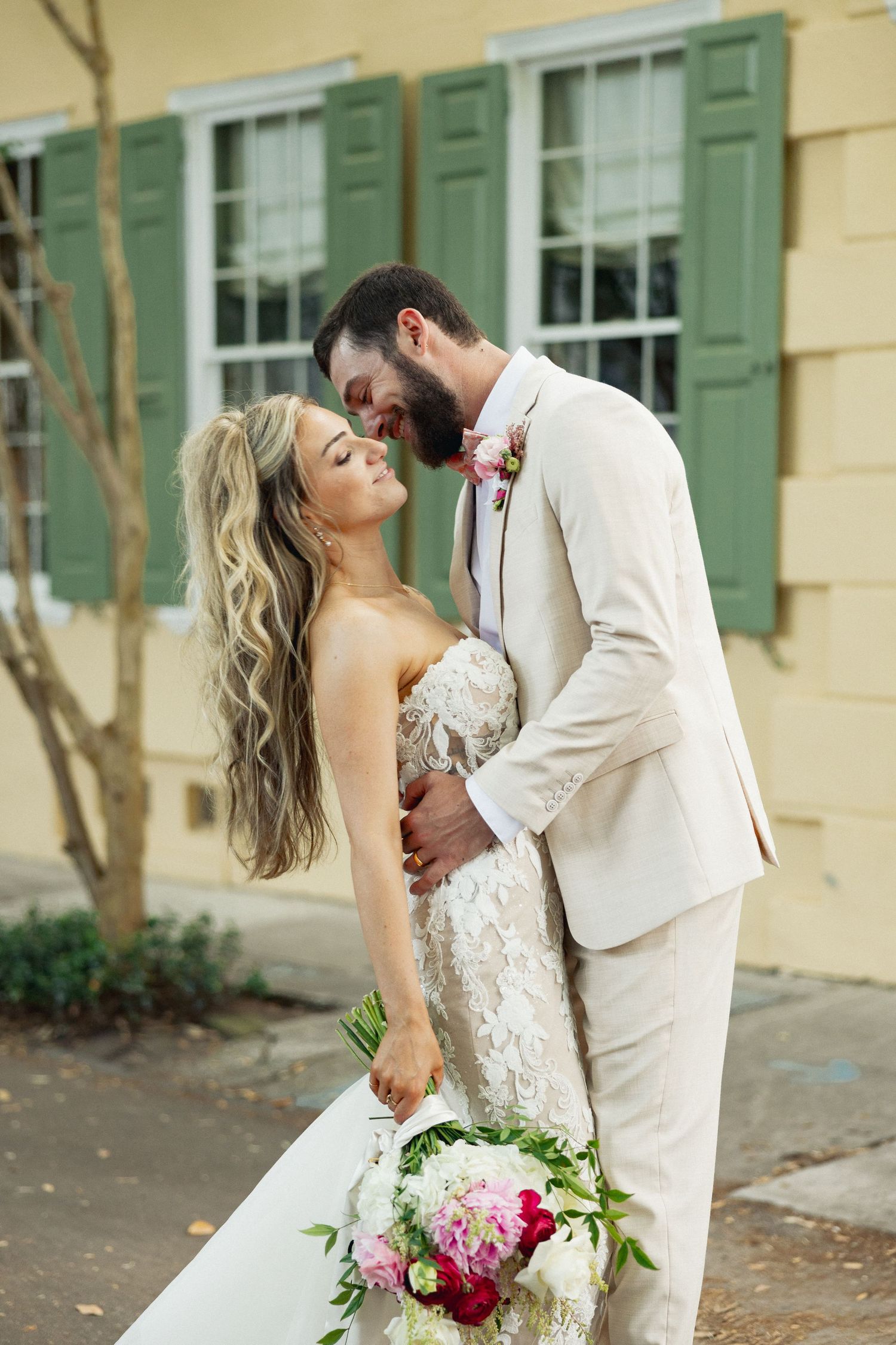 Bride and groom sharing an intimate moment outside a yellow building, bride holding a lush bridal bouquet.