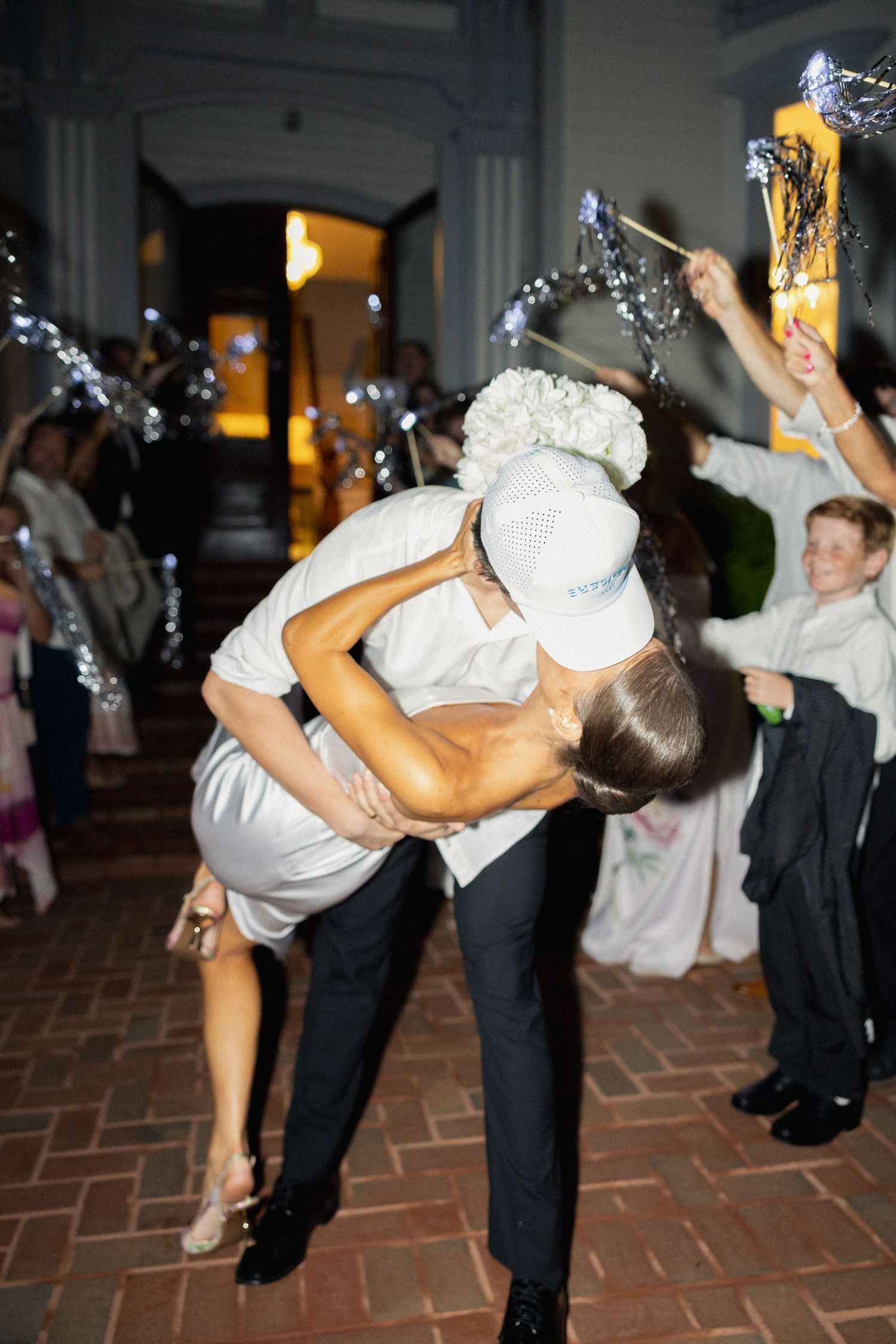 Groom dips bride for kiss during festive sparkler exit at evening wedding celebration.