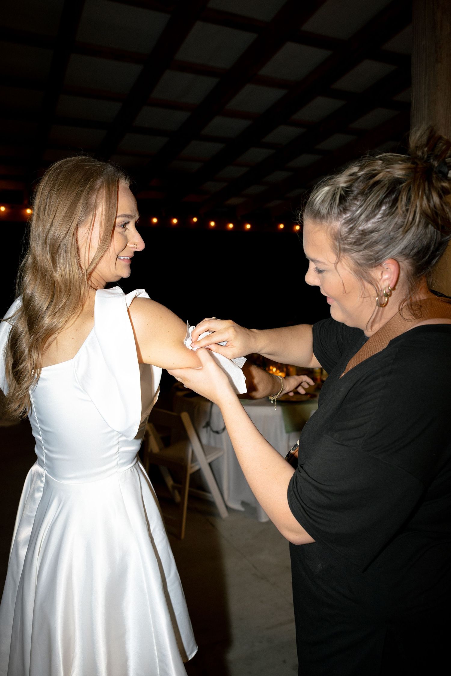 Wedding coordinator applies a temporary tattoo to the bride's arm at an evening barn reception.