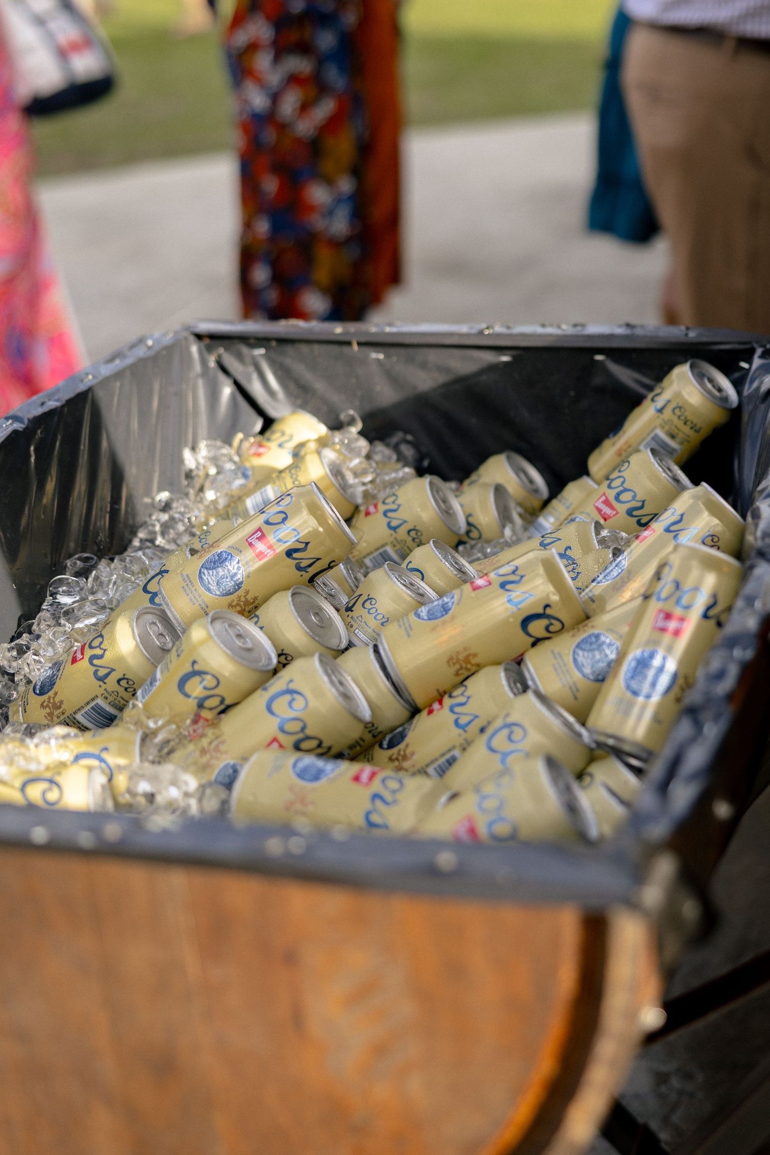 Coors Light beer cans chilling on ice in a barrel cooler at an outdoor wedding reception.