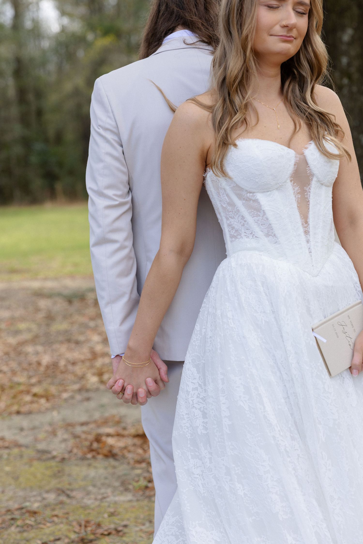 Bride and groom hold hands outdoors, bride wearing strapless lace wedding gown with sheer corset bodice.
