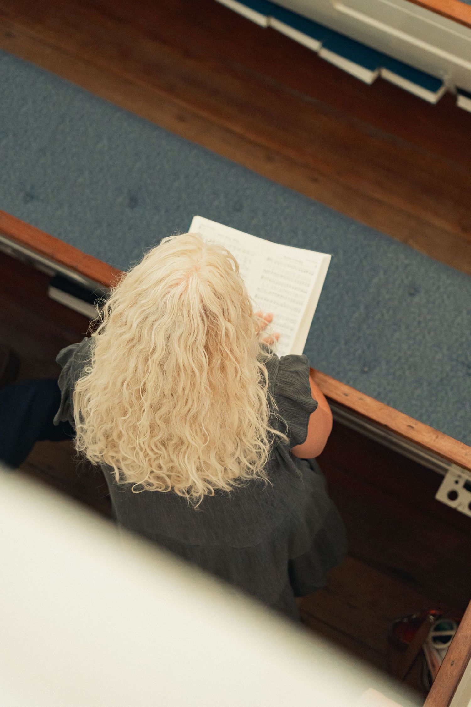 Aerial view of a blonde woman with curly hair reading a book while seated in a church pew.