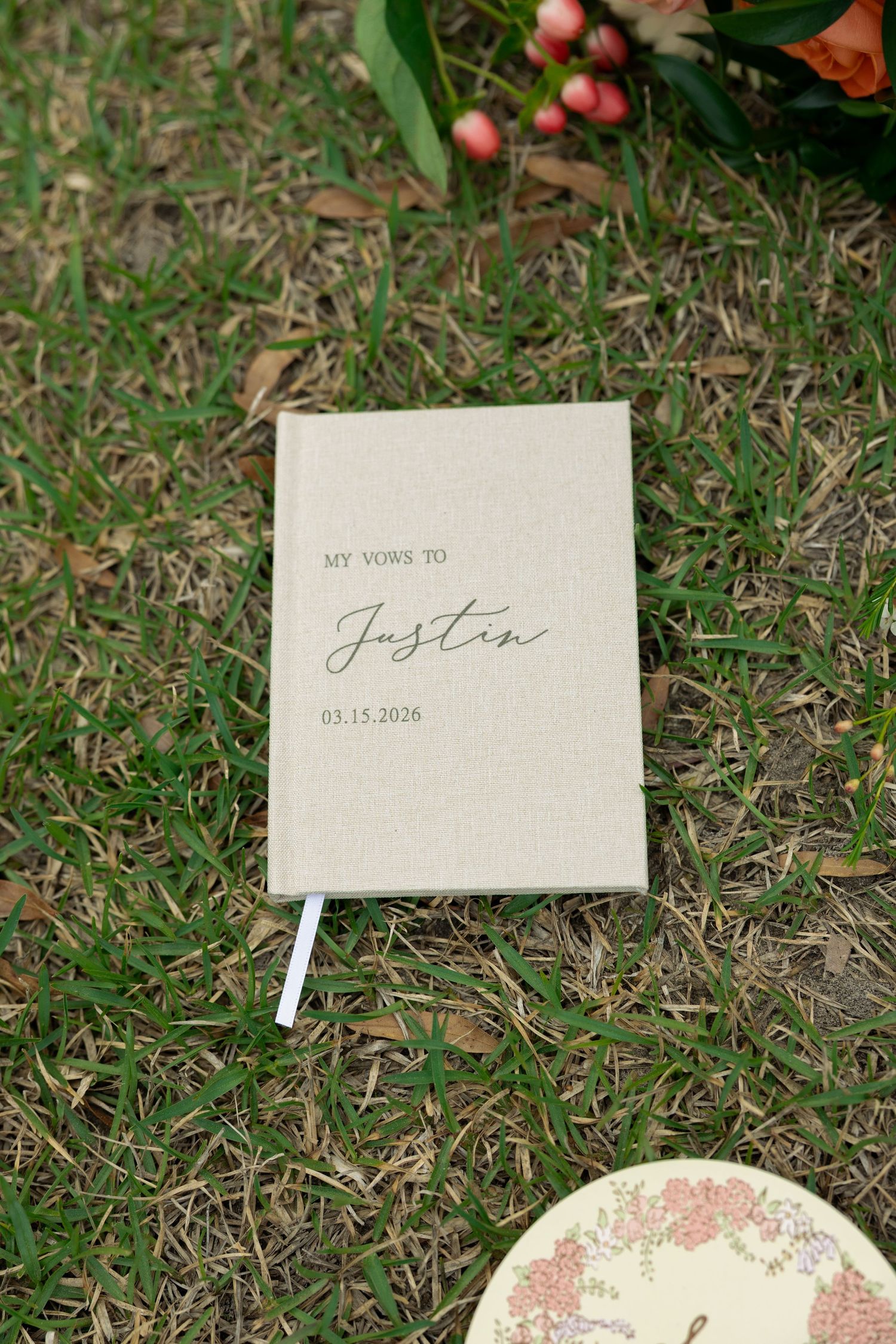 Personalized linen wedding vow book inscribed with My Vows to Justin dated 03.15.2026 on green grass.