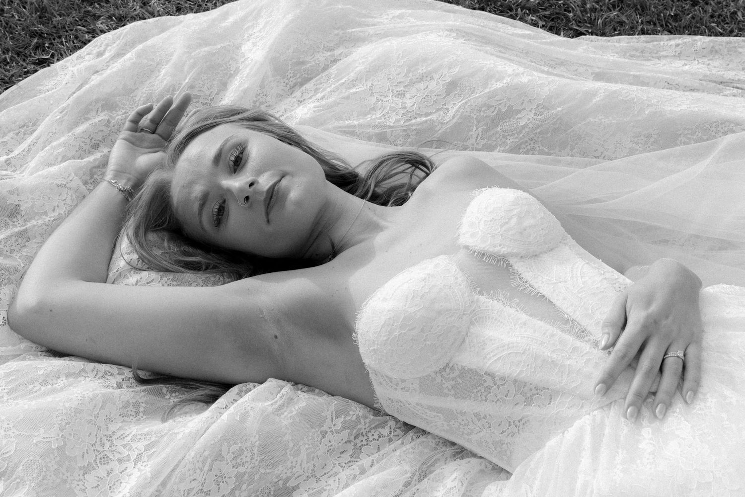 Black and white artistic photo of bride lying on tulle veil wearing strapless lace wedding gown.