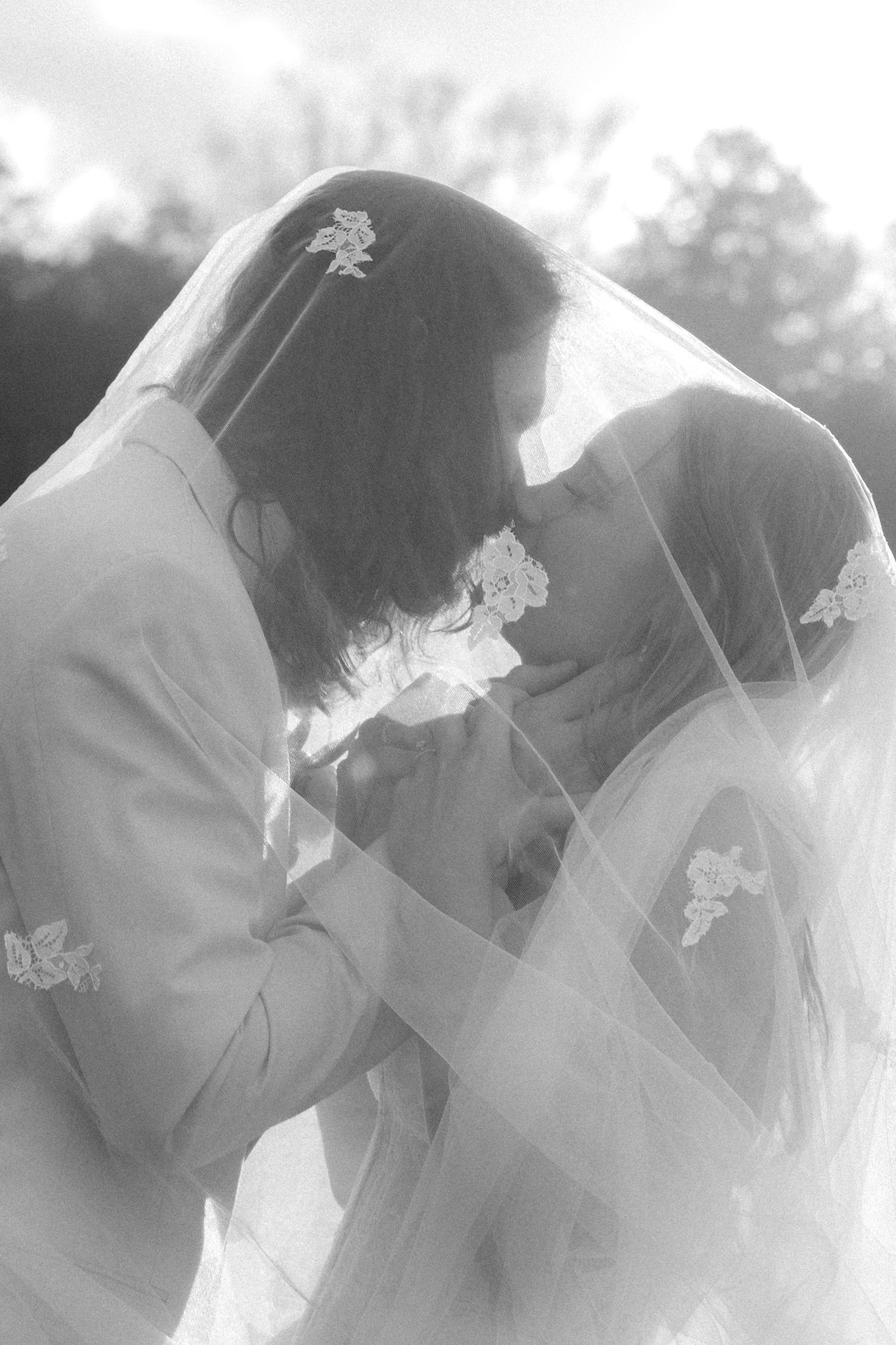 Black and white photo of bride and groom sharing intimate moment beneath floral veil.