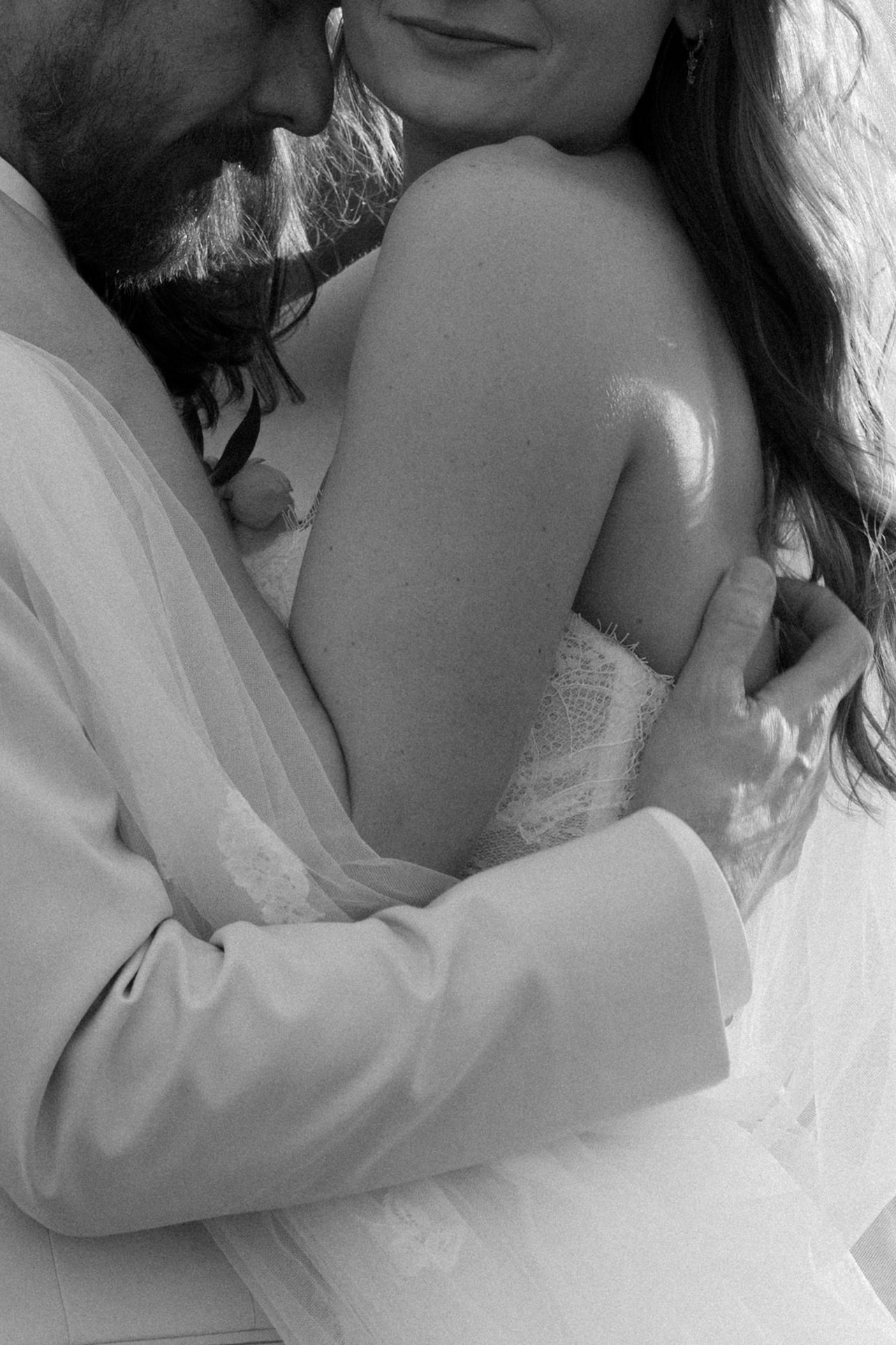Black and white close-up of groom tenderly embracing bride in strapless wedding gown.