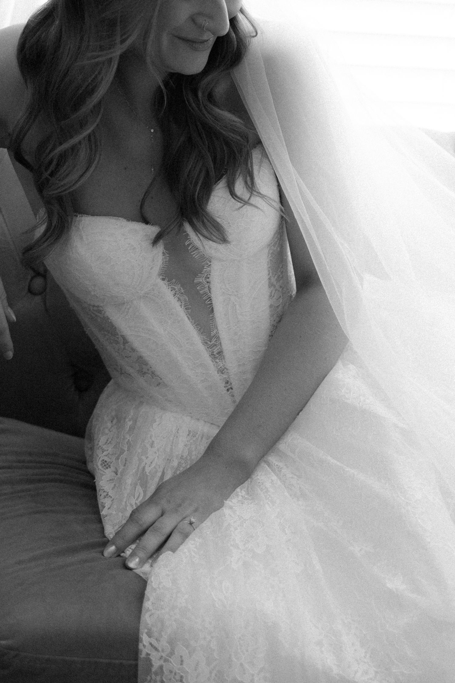 Black and white photo of bride in lace wedding dress and veil seated, showing engagement ring.