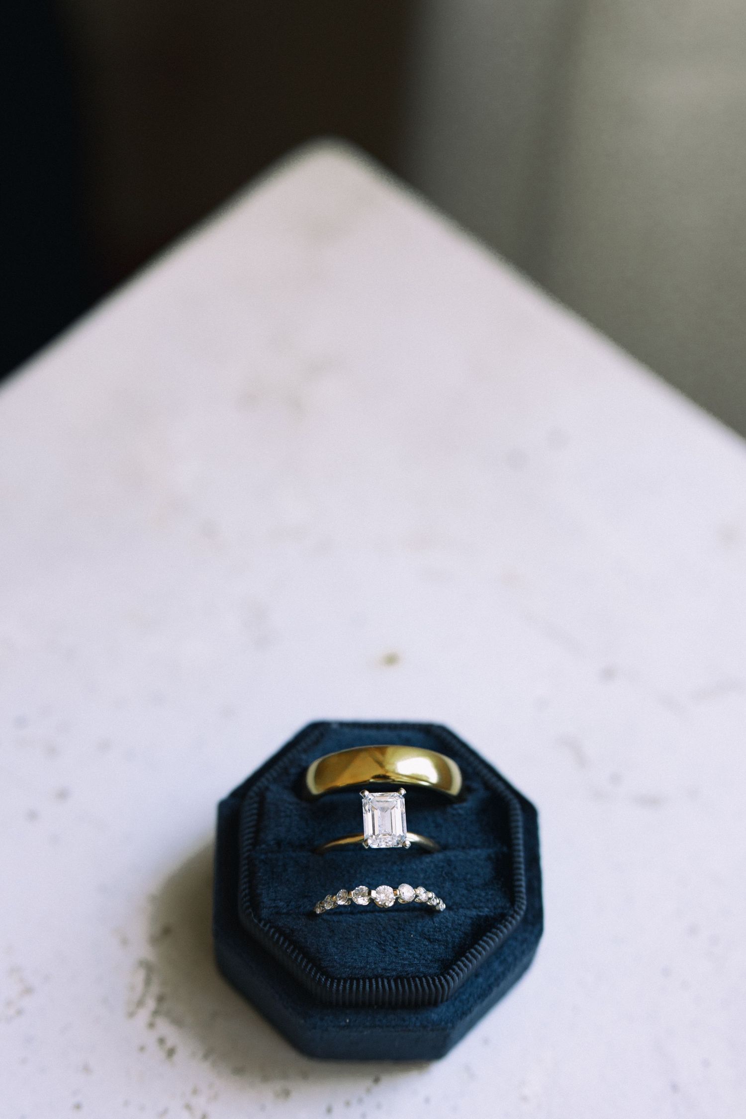 Diamond engagement ring, gold band, and diamond wedding band in navy velvet box.