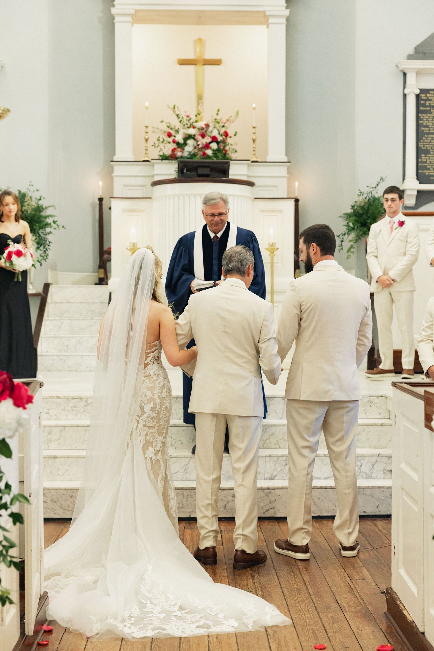 Bride and groom exchange vows before a minister at a decorated church altar with a cross.