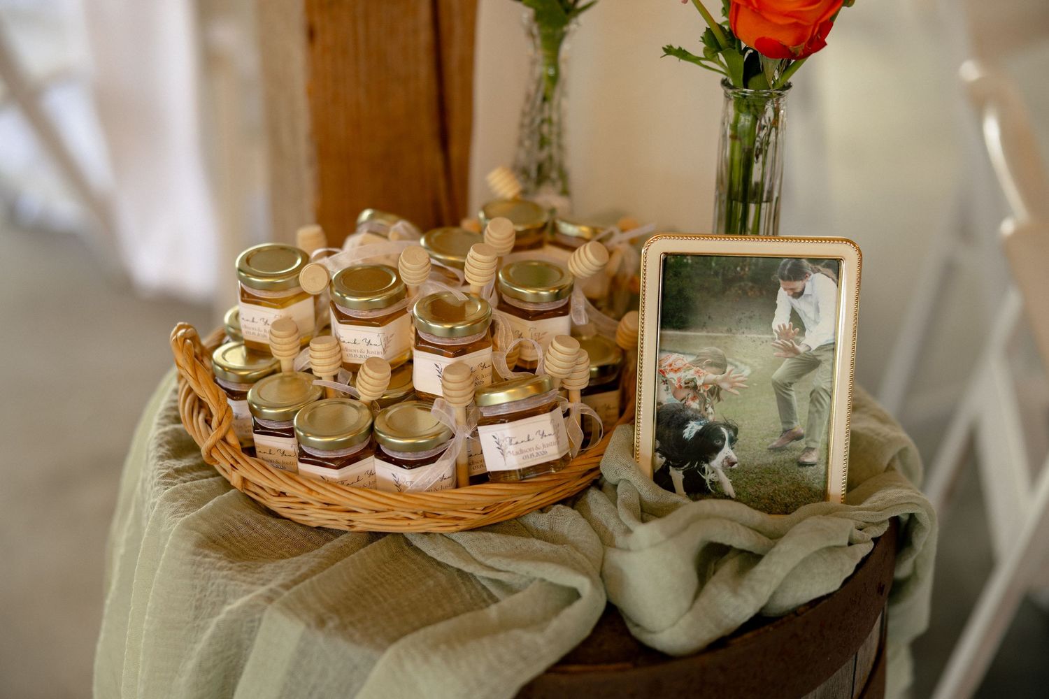 Rustic wedding favor display with small honey jars in a wicker basket beside a framed photo.