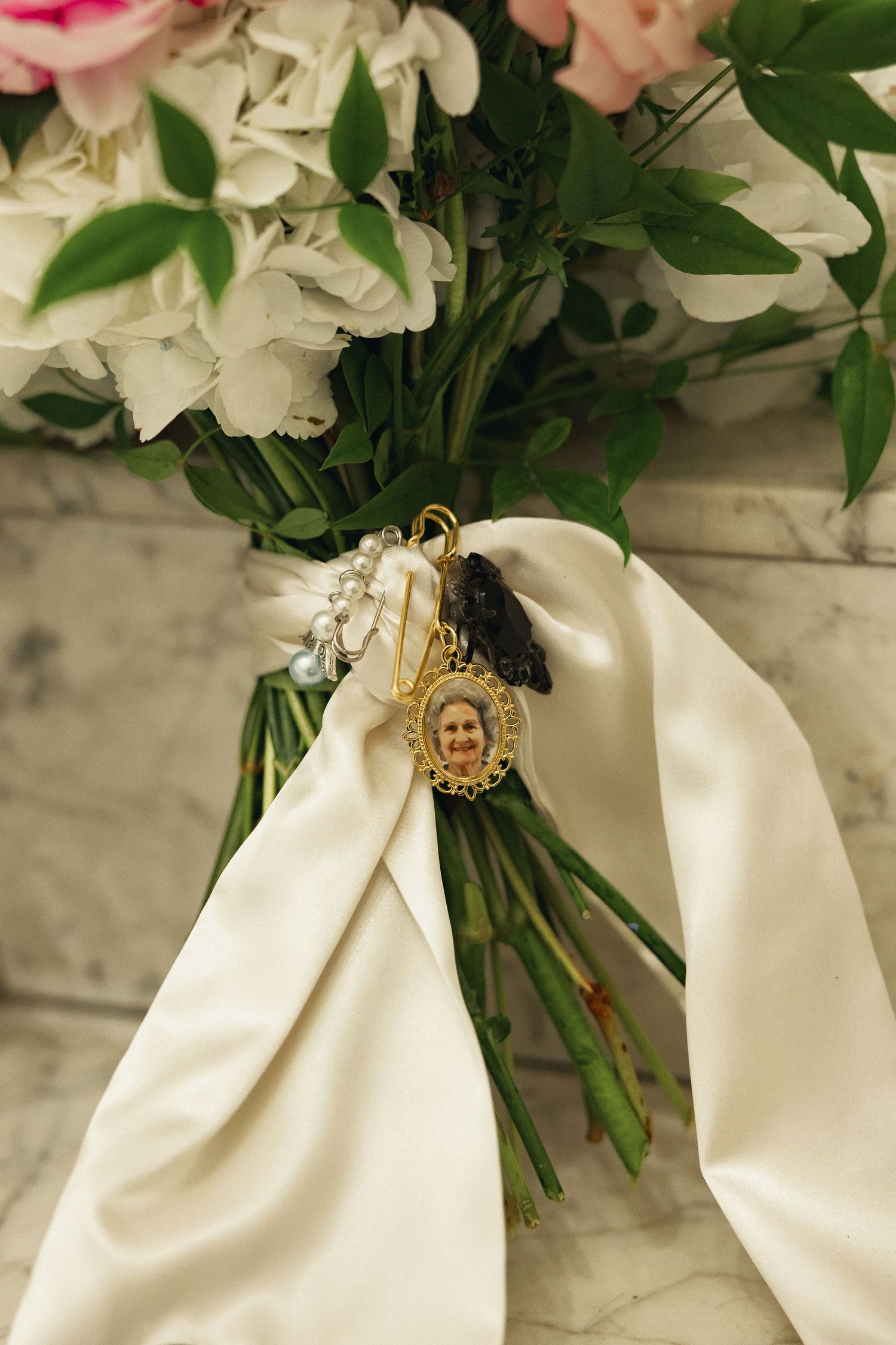 Bridal bouquet with white hydrangeas and pink roses, adorned with a gold memorial photo charm and white satin ribbon.