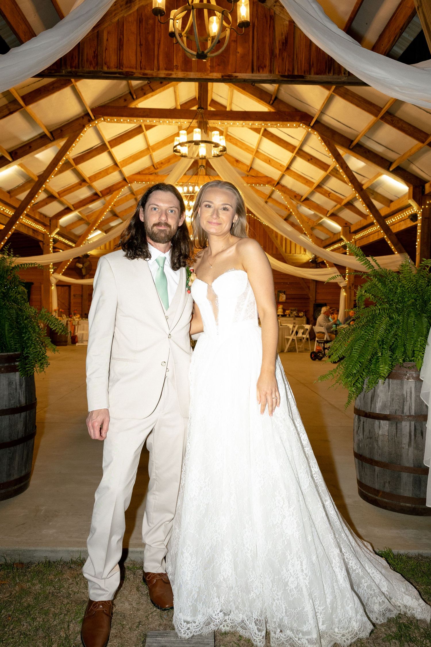 Bride and groom posing in rustic barn wedding venue with string lights.