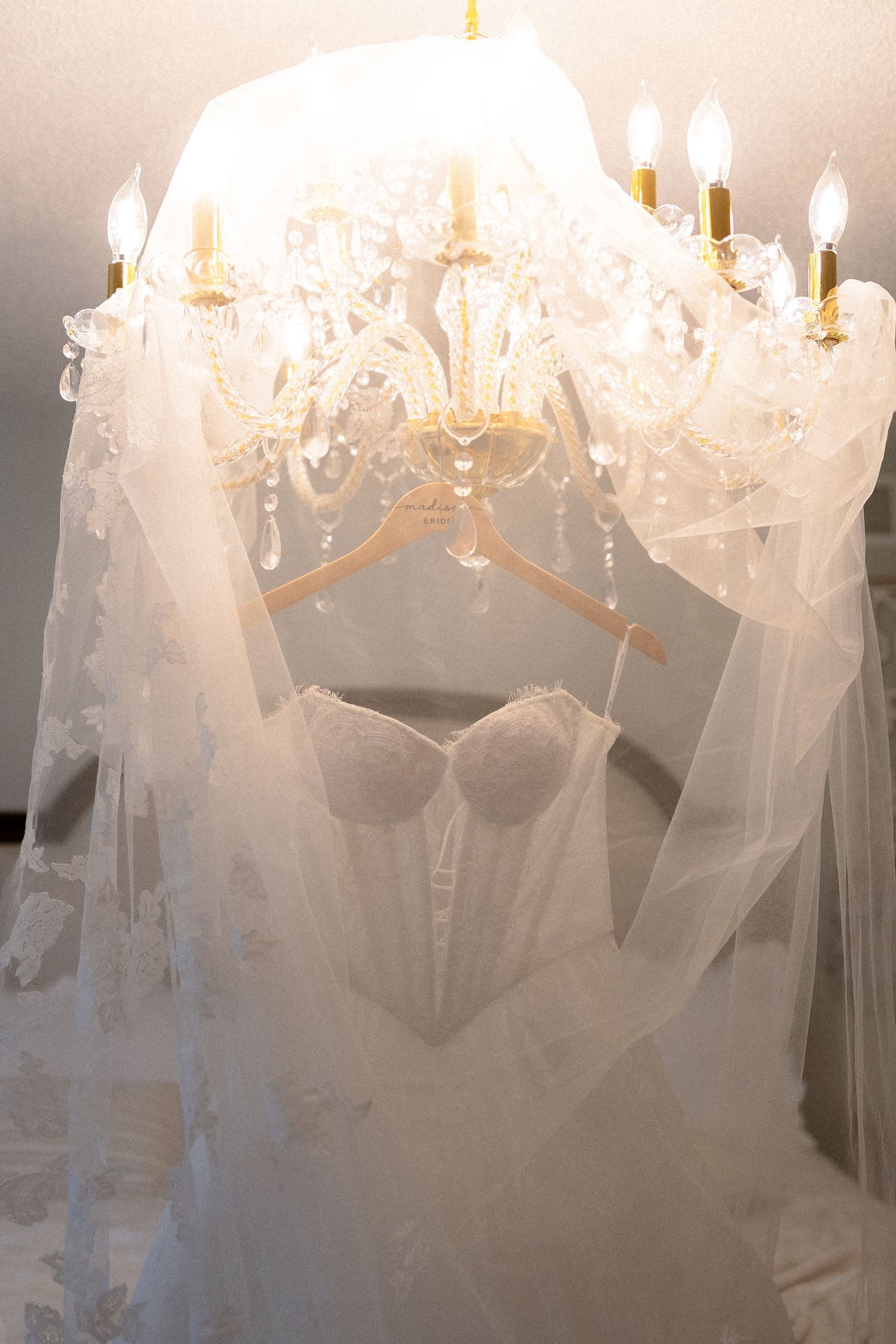 Elegant white wedding dress hanging from a crystal chandelier with candle lights and flowing veil.