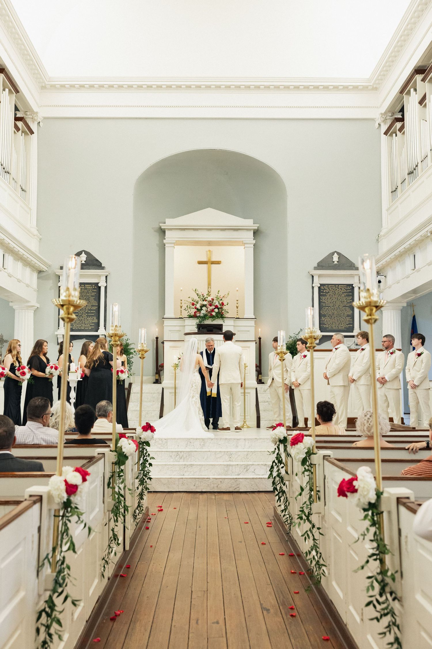 Wide view of a church wedding ceremony with bridesmaids, groomsmen, and guests seated in pews.