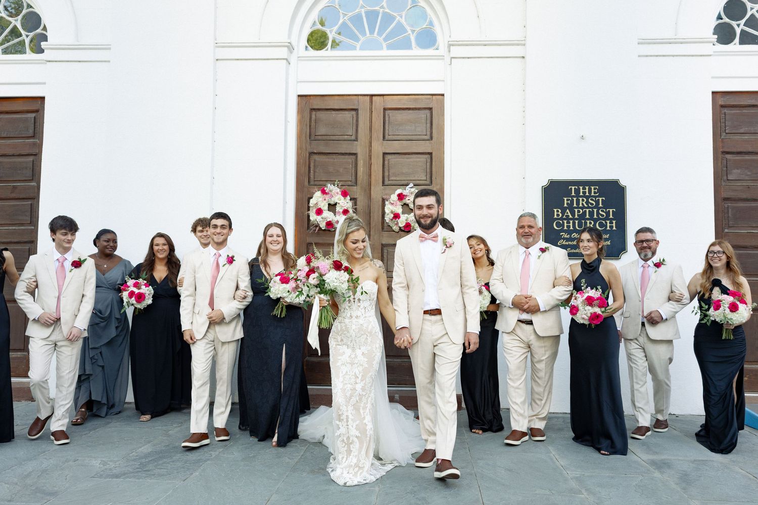 Wedding party in cream suits and black dresses pose outside First Baptist Church.