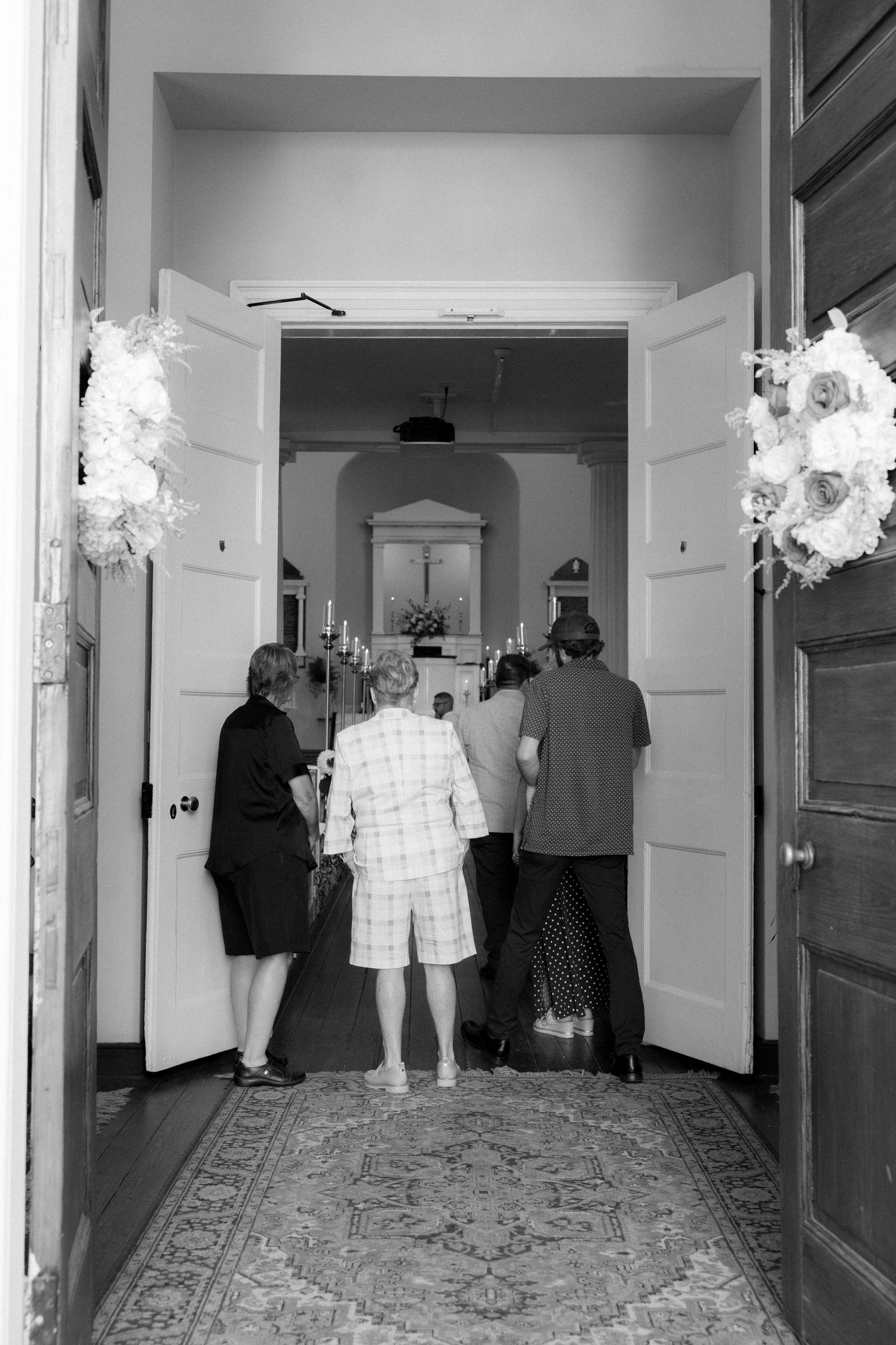Guests entering a flower-adorned church doorway for a wedding ceremony.