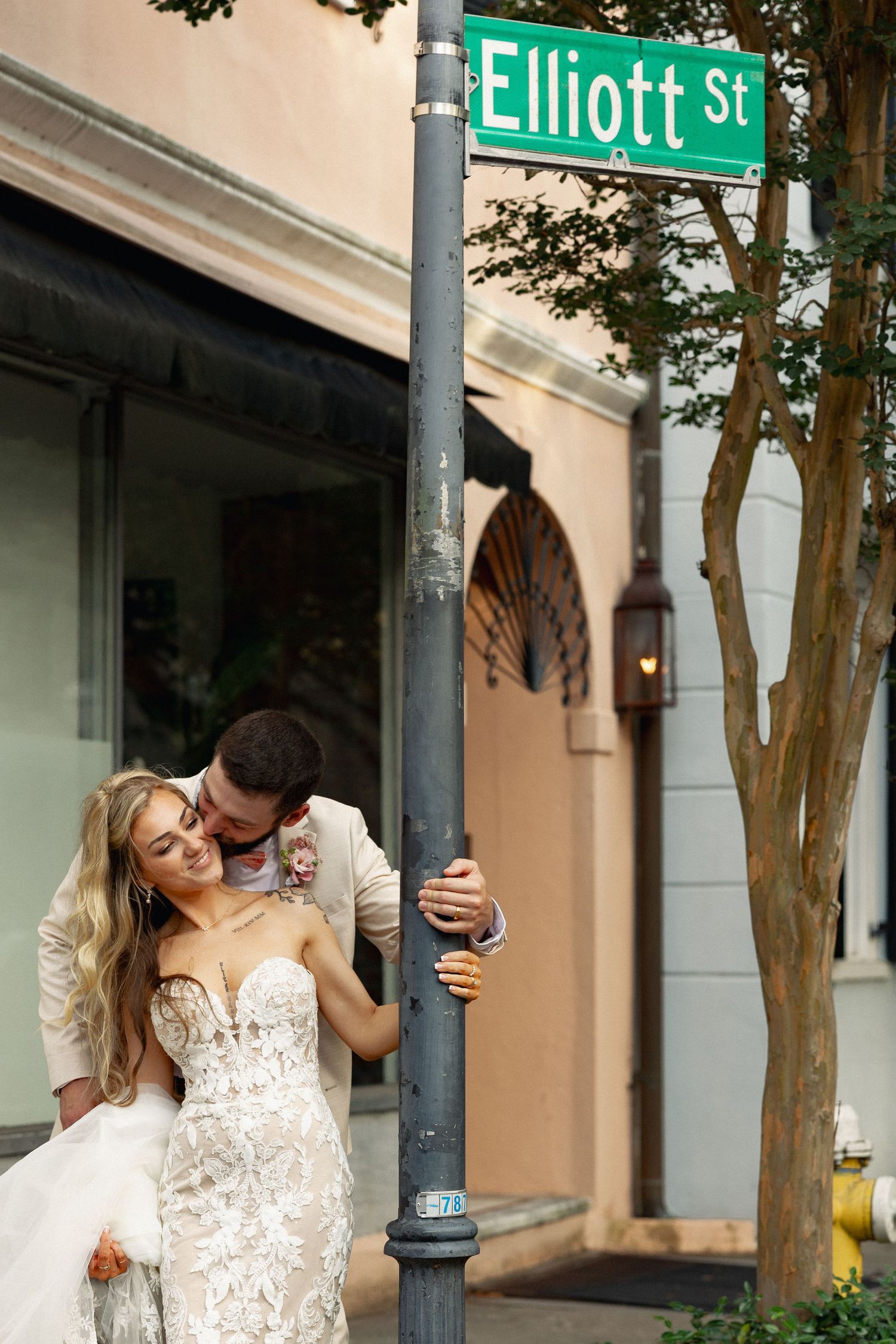 Bride and groom embracing tenderly beneath a green Elliott St street sign in a charming urban setting.
