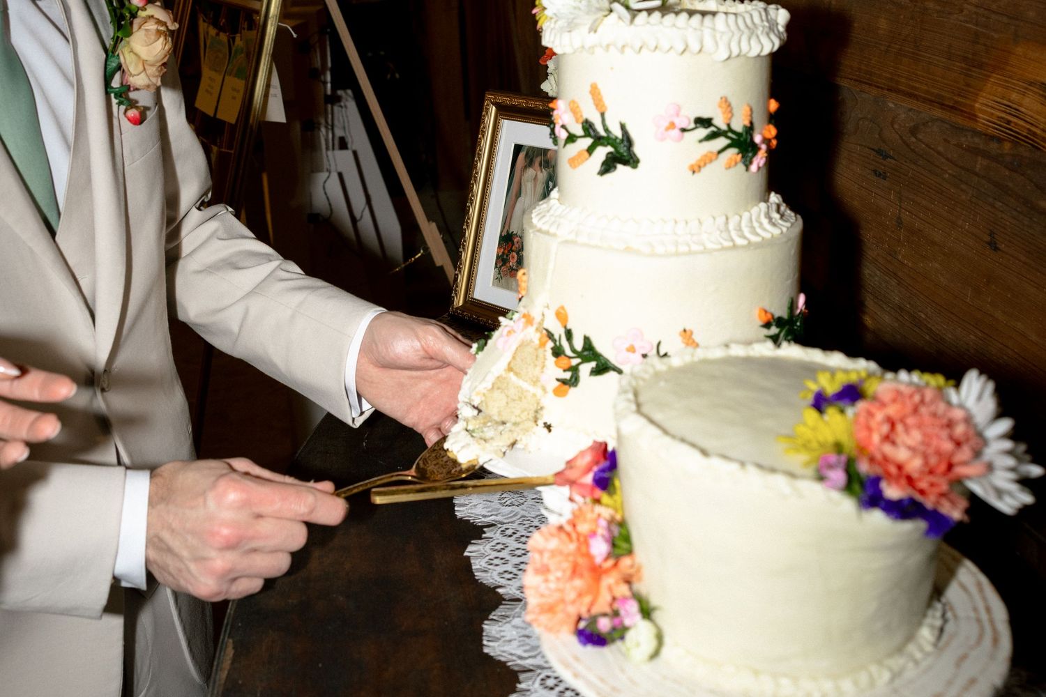 Close-up of couple cutting two-tier white wedding cake decorated with colorful flowers at reception.