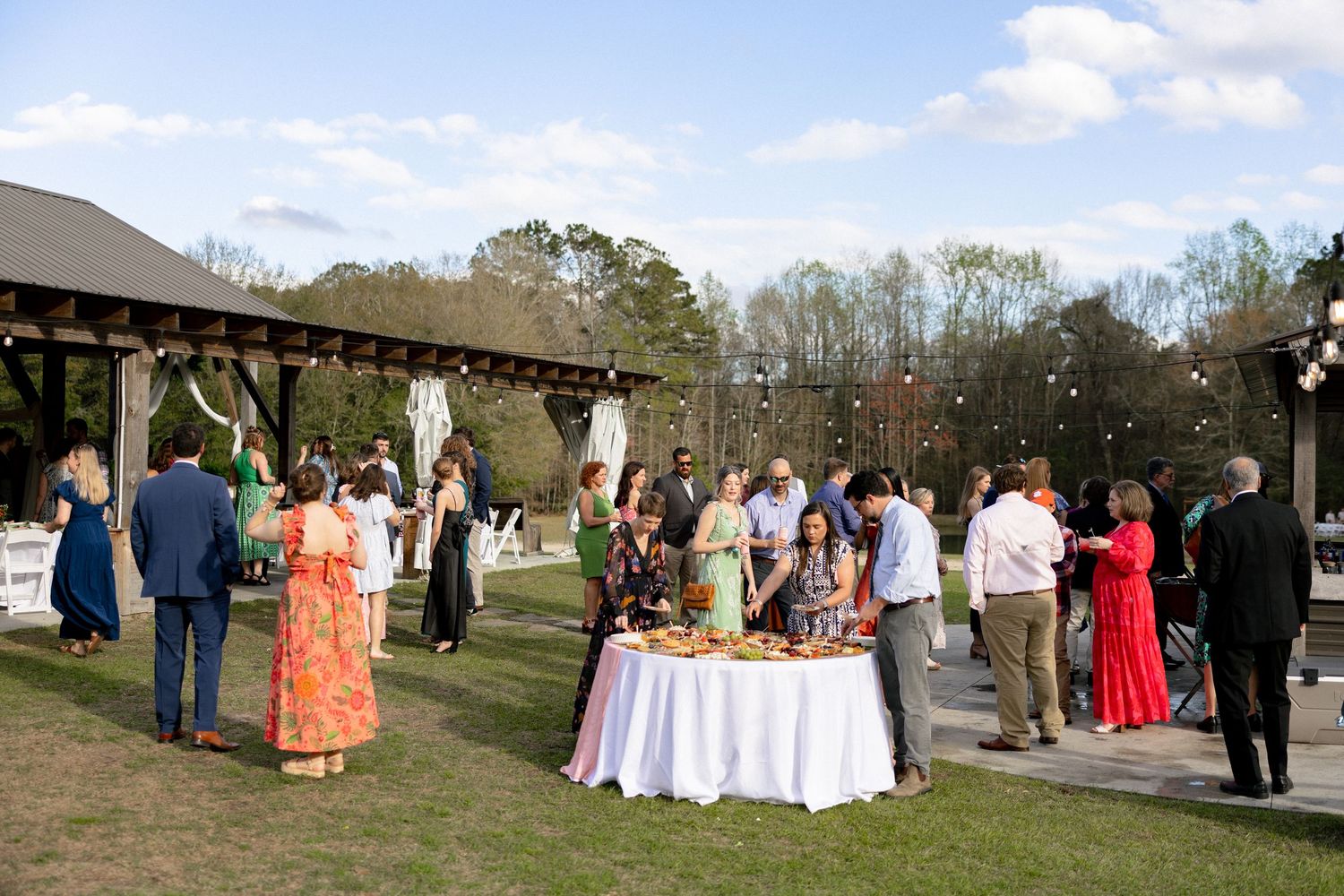 Guests mingling outdoors at a wedding cocktail hour on a green lawn with string lights.