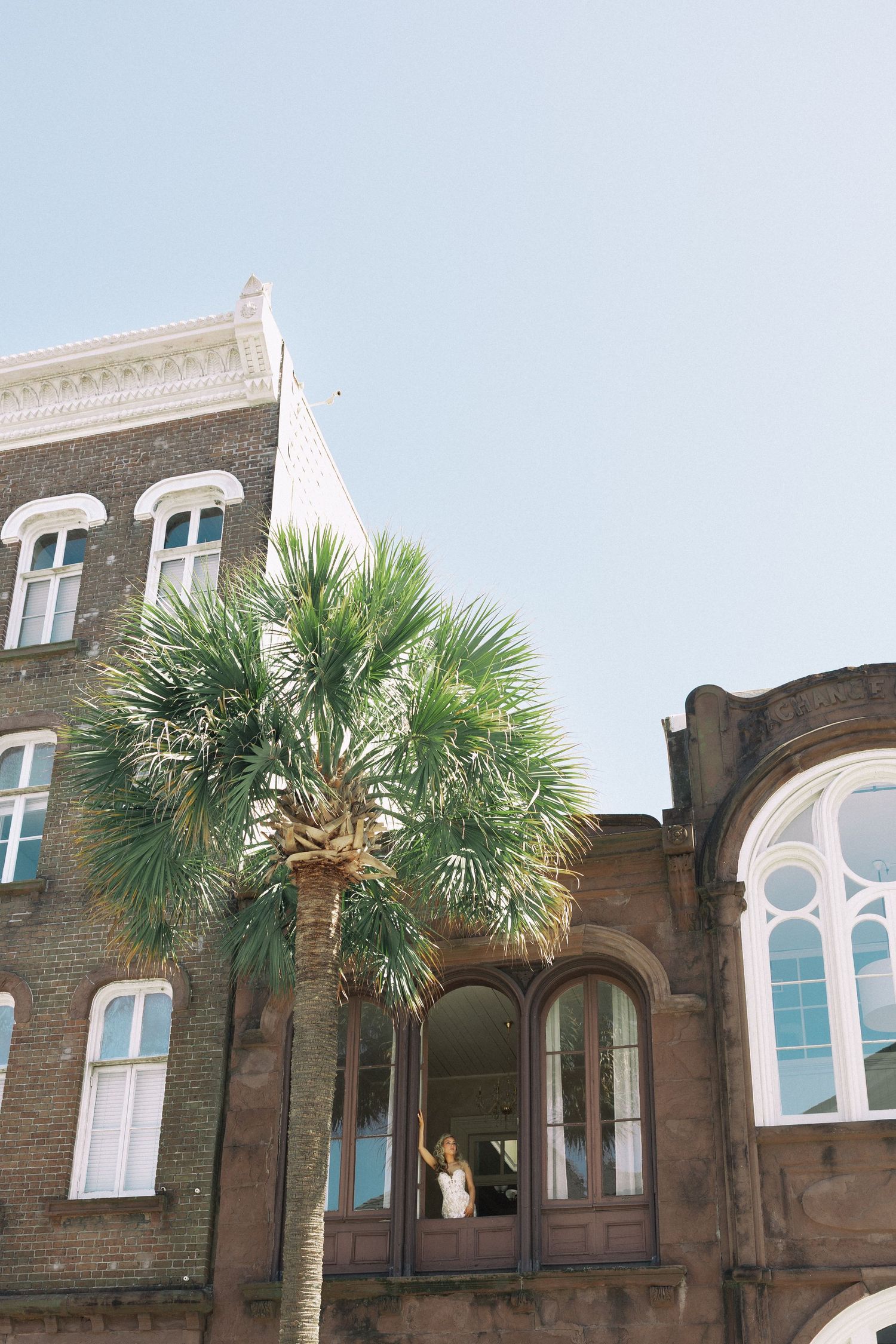 Bride standing in doorway of historic brick building with palm tree in Charleston, SC.