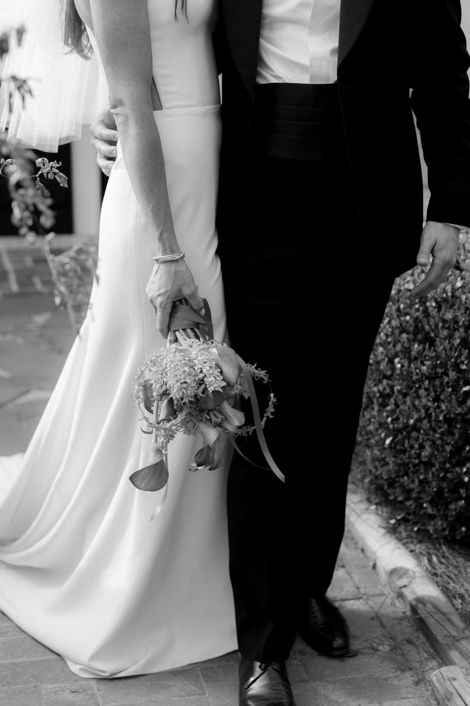 Black and white photo of bride and groom standing close, bride holding delicate floral bouquet at side.