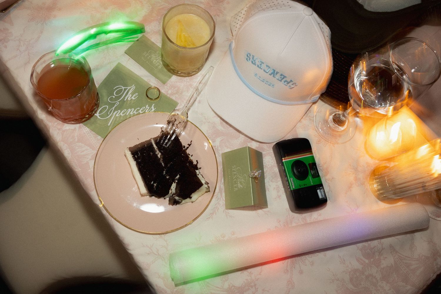 Party table with glowing LED sticks, cocktails, a white hat, smartphone, and personalized Spencer's name card.