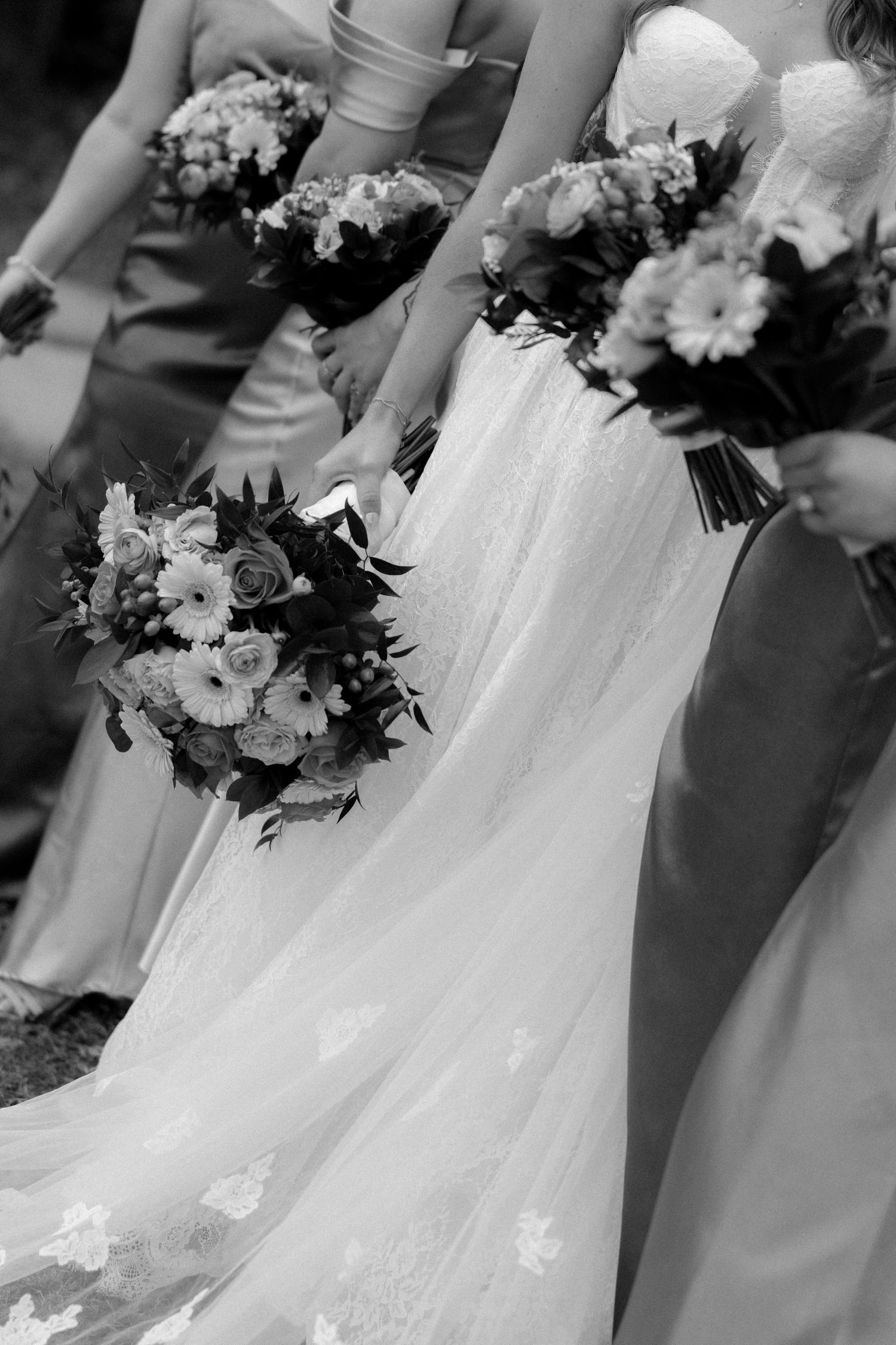 Black and white close-up of bride and bridesmaids holding lush floral bouquets with flowing gown train.
