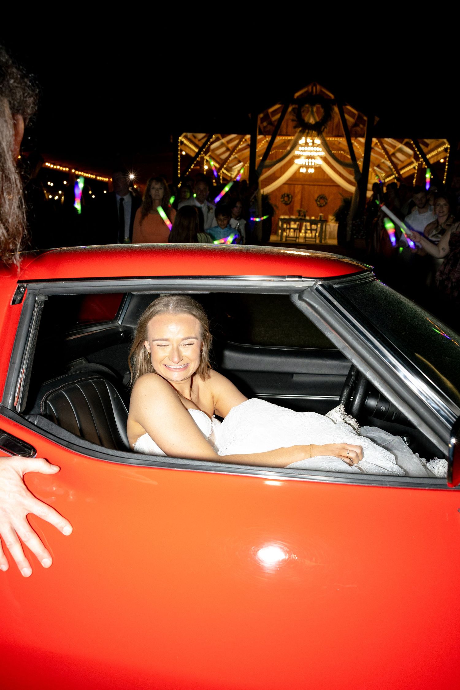 Smiling bride sitting in red vintage convertible car after wedding reception.