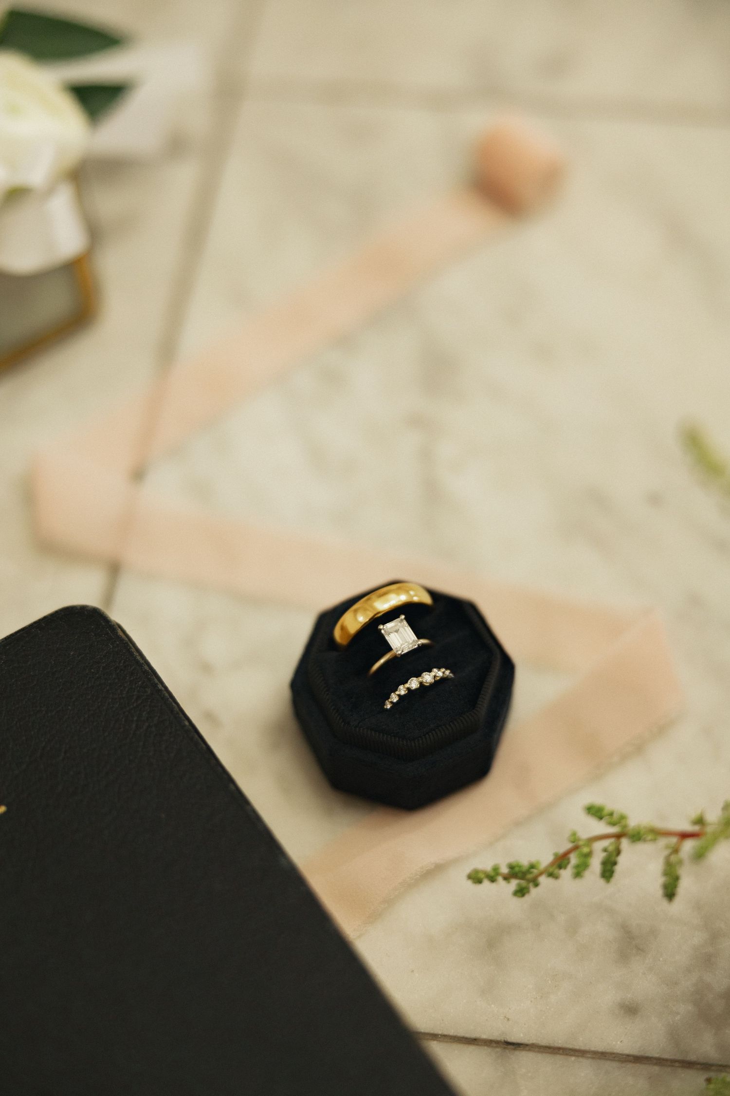 Gold wedding bands and diamond engagement ring displayed in a black velvet ring box on marble surface.